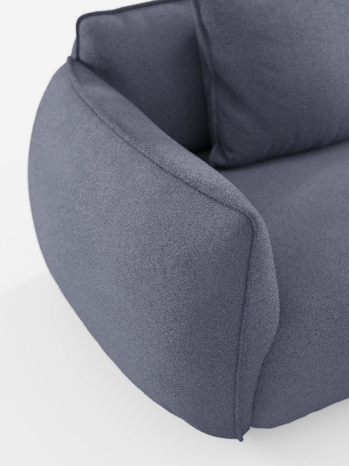 Primo piano del divano angolare con penisola componibile Nimbus di Divani.Store, che mette in risalto il suo tessuto effetto cotone (T33) dal motivo testurizzato, di colore grigio medio e resistente alle macchie. Il bracciolo curvo e imbottito si fonde con il cuscino di seduta e lo schienale spessi, incarnando il suo design minimalista e contemporaneo. Il divano è presentato su una superficie bianca senza gambe visibili.