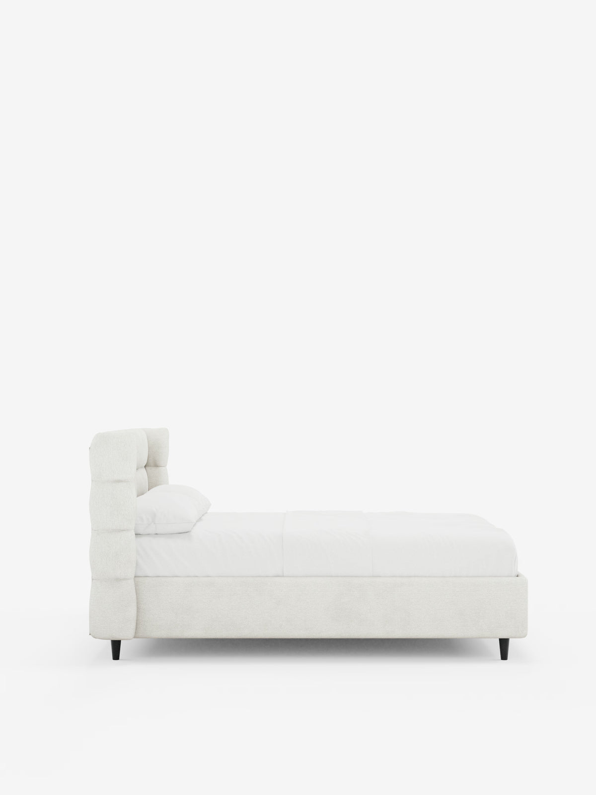 Vista laterale del letto imbottito RAGNAR con contenitore e testiera capitonné avvolgente di Letti.store, caratterizzato da un’alta testiera imbottita avvolgente realizzata in un elegante tessuto bianco sporco certificato Oeko-Tex®. Il letto è abbinato a biancheria da letto bianca e a un unico cuscino, ed è sostenuto da gambe corte e scure. È posizionato su uno sfondo bianco a tinta unita per enfatizzarne il design pulito e minimalista.