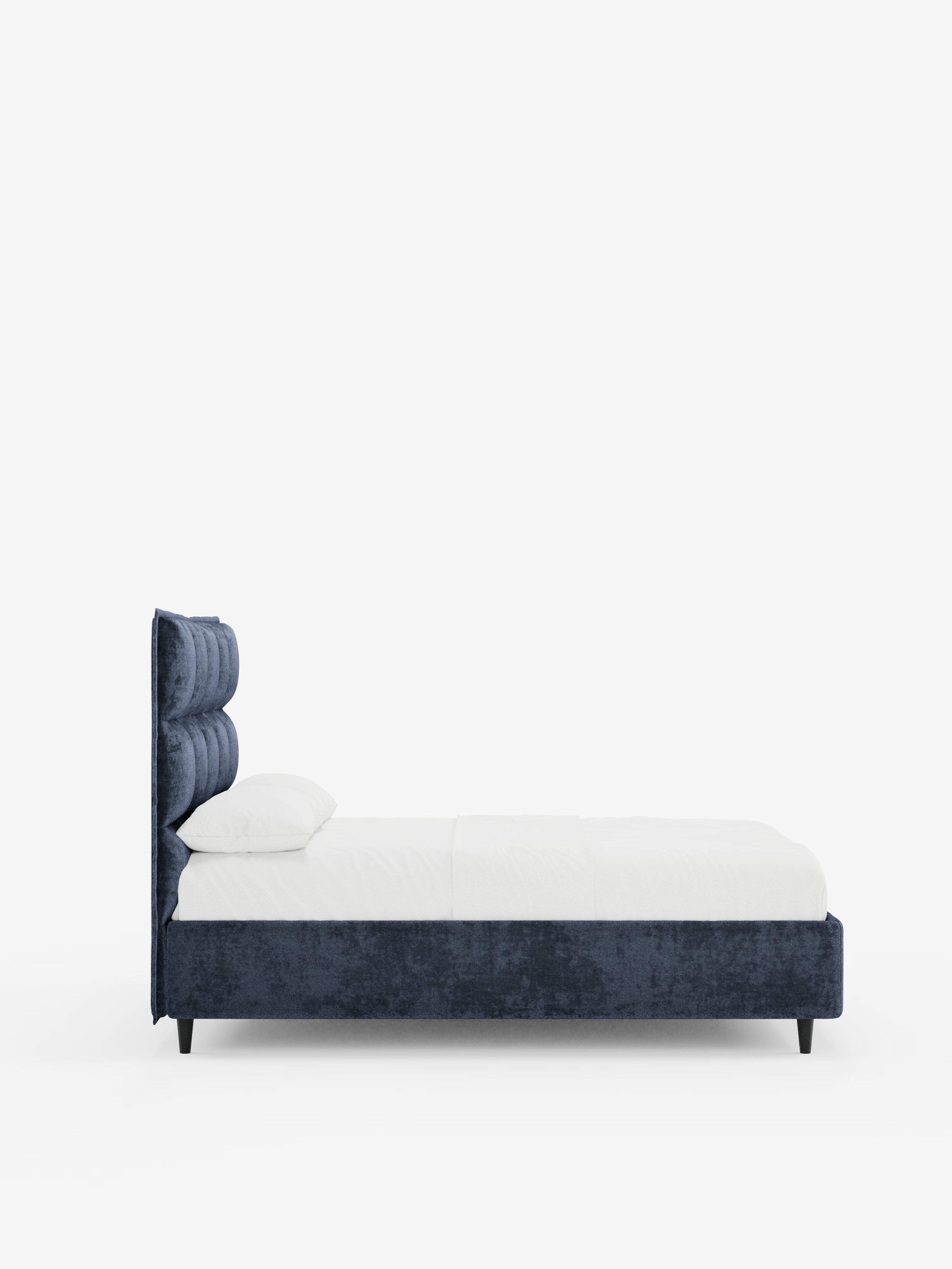 Vista laterale del letto imbottito AURO con contenitore e testiera alta capitonné in ciniglia Oeko-Tex® di Letti.store, caratterizzato da una testiera alta capitonné e da una struttura coordinata in blu navy. Il letto è dotato di materasso e cuscini bianchi, poggia su corte gambe nere ed è esposto su uno sfondo bianco a tinta unita: ideale per camere dal design contemporaneo.