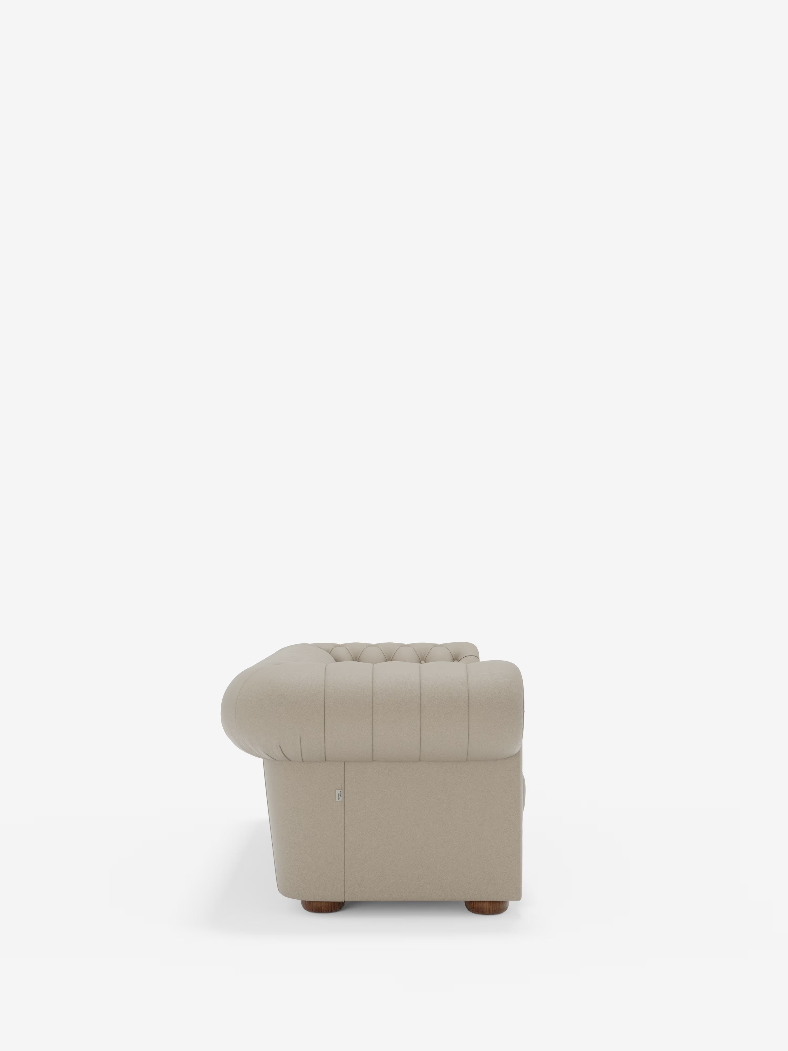 Vista laterale della Chester – Divano Chesterfield in vera pelle spessorata a 2 e 3 posti di Divani.Store, qui raffigurata in beige. Questa elegante poltrona, ispirata al classico design Chesterfield, presenta braccioli arrotondati, cuciture verticali e piedini in legno. Fotografata su uno sfondo bianco a tinta unita, l’immagine mette in risalto il bracciolo e parte della seduta.