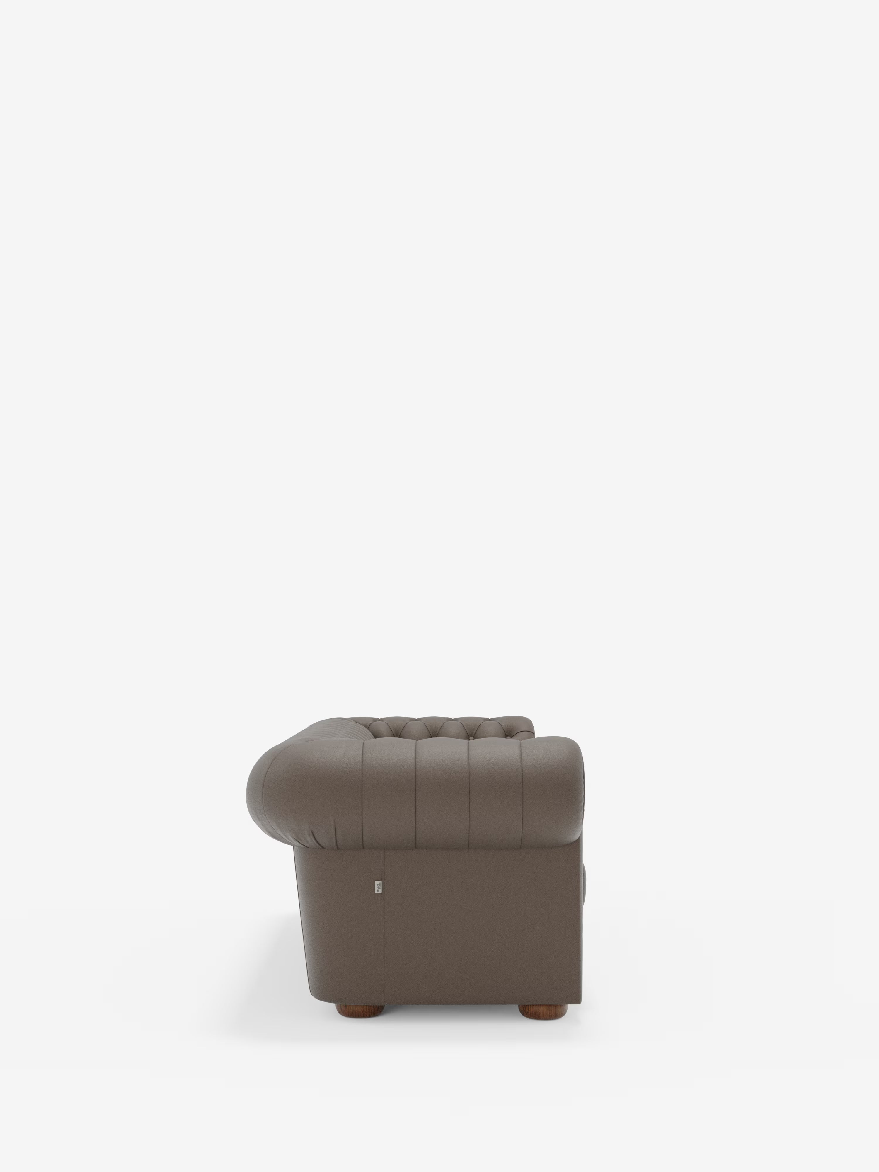 Un divano in pelle marrone con capitonné — il modello Chester di Divani.Store, un divano Chesterfield in vera pelle spessorata disponibile nelle versioni a 2 e 3 posti — è ripreso di profilo su uno sfondo bianco a tinta unita. Spiccano i braccioli e lo schienale arrotondati, mentre alla base si intravedono i delicati piedini in legno. Il design classico richiama lo stile tradizionale Chesterfield, con cuciture pulite sul rivestimento che mettono in risalto la maestria artigianale.