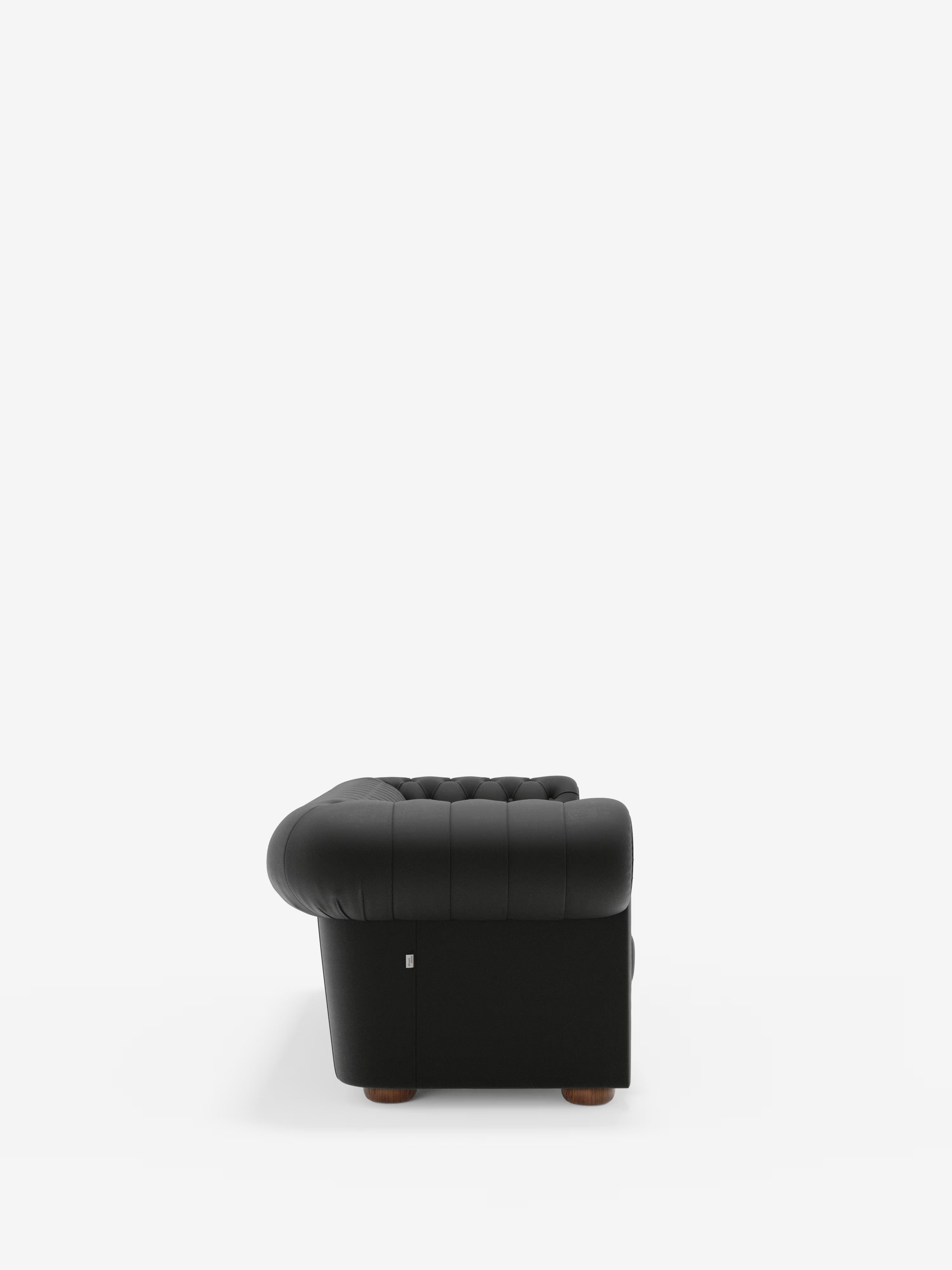 Un divano Chesterfield nero con capitonné – Divano Chesterfield in vera pelle spessorata a 2 e 3 posti di Divani.Store – è raffigurato di profilo su uno sfondo bianco a tinta unita, mettendo in risalto i braccioli arrotondati, lo schienale imbottito e le gambe corte in legno. Questo divano Chesterfield in vera pelle spessorata incarna l’eleganza classica e l’eccezionale maestria artigianale: un vero divano artigianale made in Italy.
