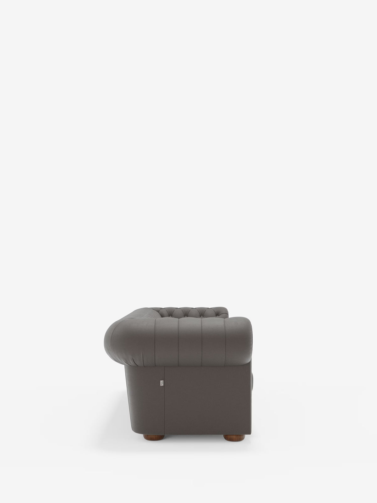 Un divano Chester 4 Posti 3 sedute in vera pelle, colore grigio scuro – Chesterfield Capitonné Artigianale di Divani.Store, visto di profilo, mette in risalto i braccioli e lo schienale arrotondati, le gambe in legno e una piccola etichetta metallica nell’angolo inferiore, su uno sfondo bianco a tinta unita. Questo elegante divano è orgogliosamente Made in Italy.
