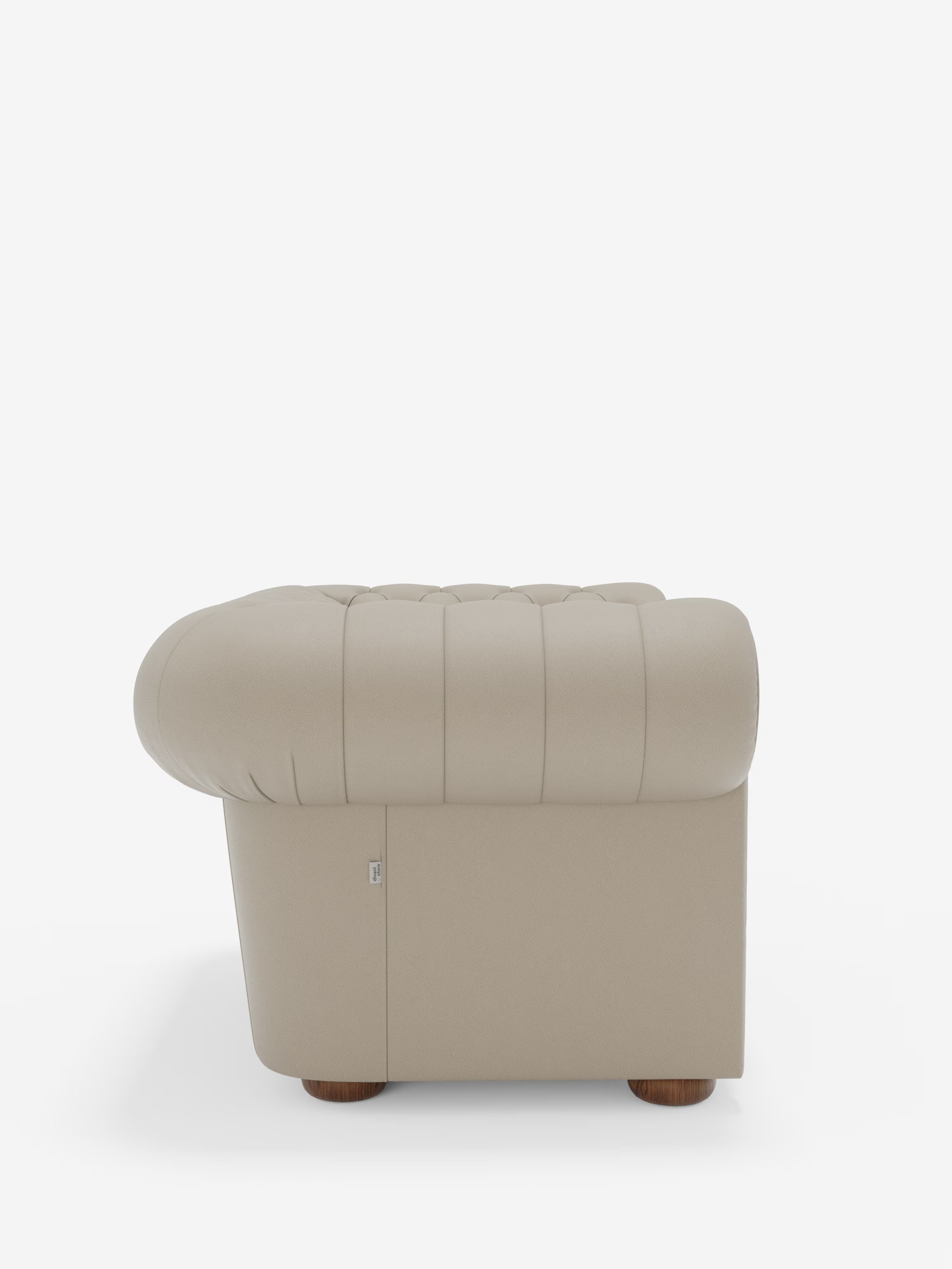 Vista laterale della poltrona Chester in vera pelle spessorata con capitonné artigianale di Divani.Store, una lussuosa poltrona beige ispirata al classico design Chester. Presenta braccioli arrotondati, schienale basso e gambe in legno, il tutto su uno sfondo bianco a tinta unita. Questo elegante complemento d’arredo è rifinito con capitonné artigianale e sottili dettagli di cuciture verticali sul rivestimento in pelle spessa di alta qualità.