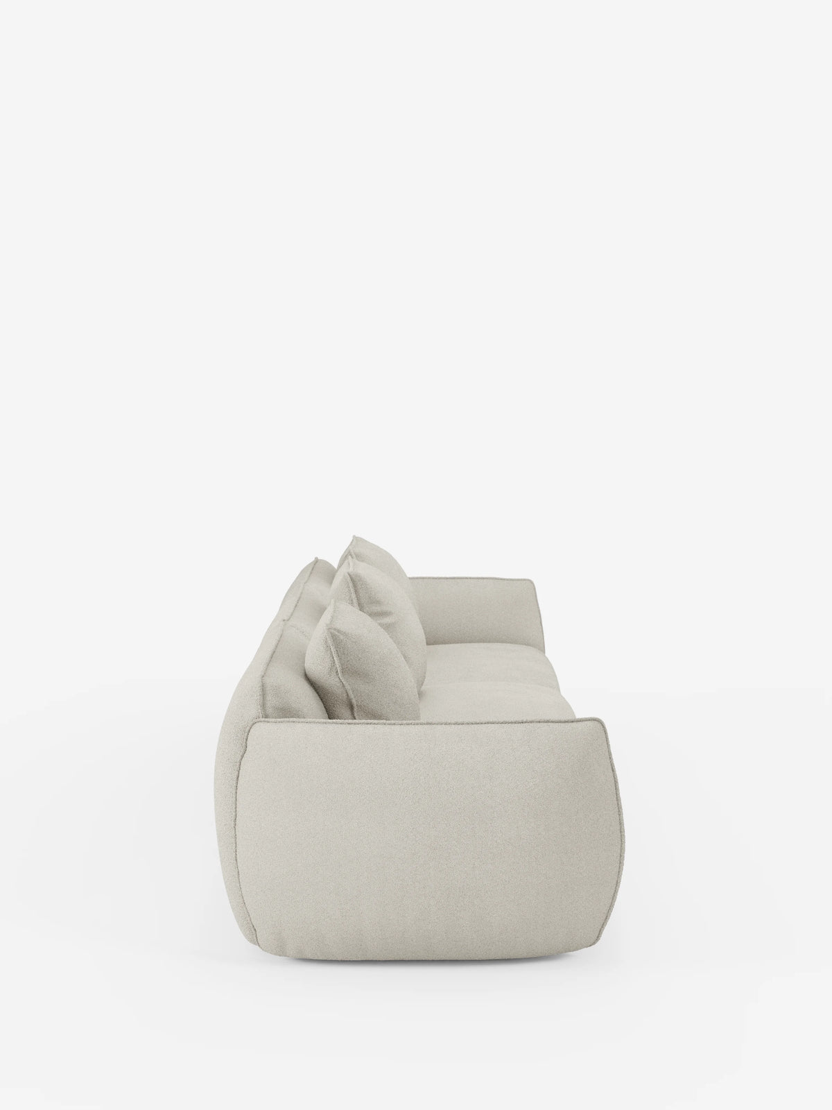 Un divano modulare Nimbus a 3 posti, in beige chiaro e dallo stile moderno, realizzato da Divani.Store, è raffigurato di profilo su uno sfondo bianco a tinta unita. Il divano presenta due grandi cuscini dello schienale, una silhouette bassa e arrotondata e un rivestimento soffice e dall’aspetto morbido in tessuto smacchiabile effetto cotone T33, caratterizzato da linee pulite e minimaliste.