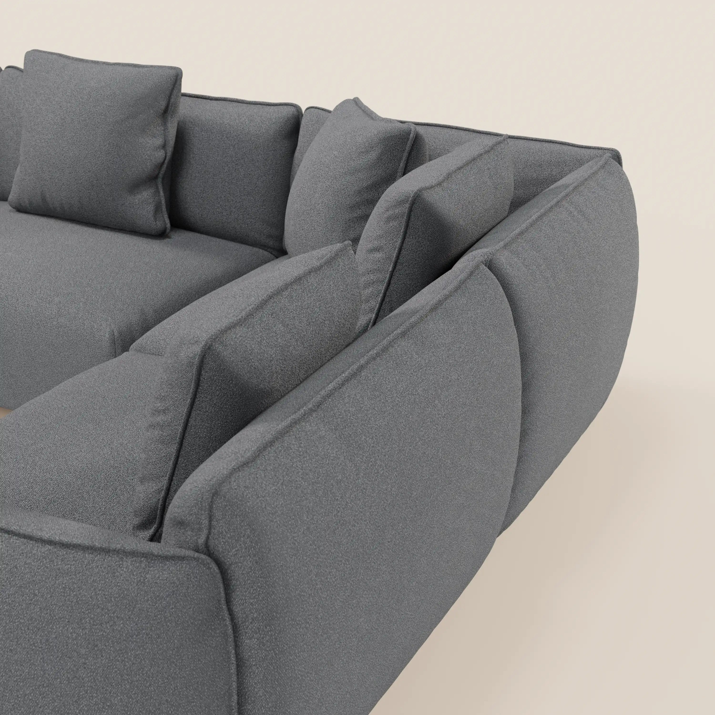 Una vista ravvicinata e angolata del divano angolare panoramico componibile Nimbus di Divani.Store in grigio, con cuscini e guanciali in tessuto antimacchia t33, mette in evidenza il suo elegante design italiano su uno sfondo beige chiaro.