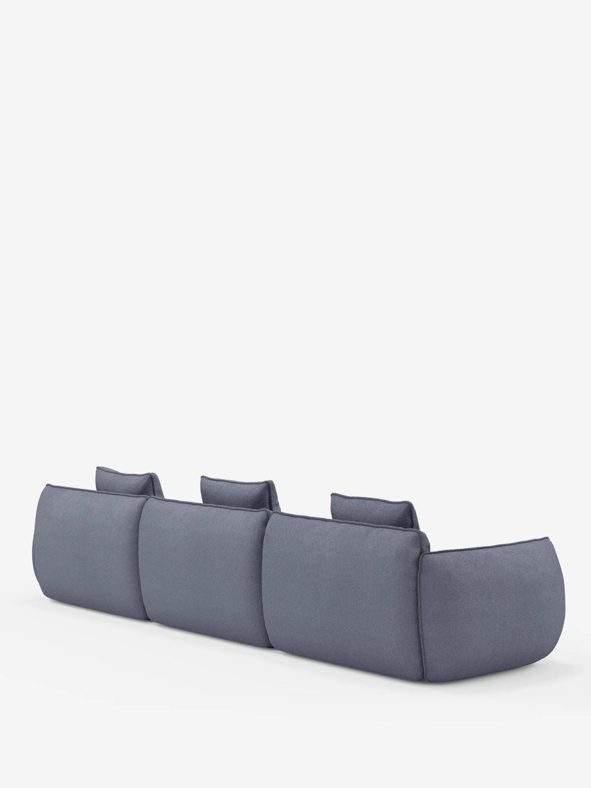 Un divano angolare a tre posti Nimbus con penisola componibile di Divani.Store, rivestito in tessuto blu-grigio effetto cotone antimacchia (T33), visto da dietro; presenta sezioni arrotondate e imbottite e tre schienali bassi, il tutto su uno sfondo bianco a tinta unita.