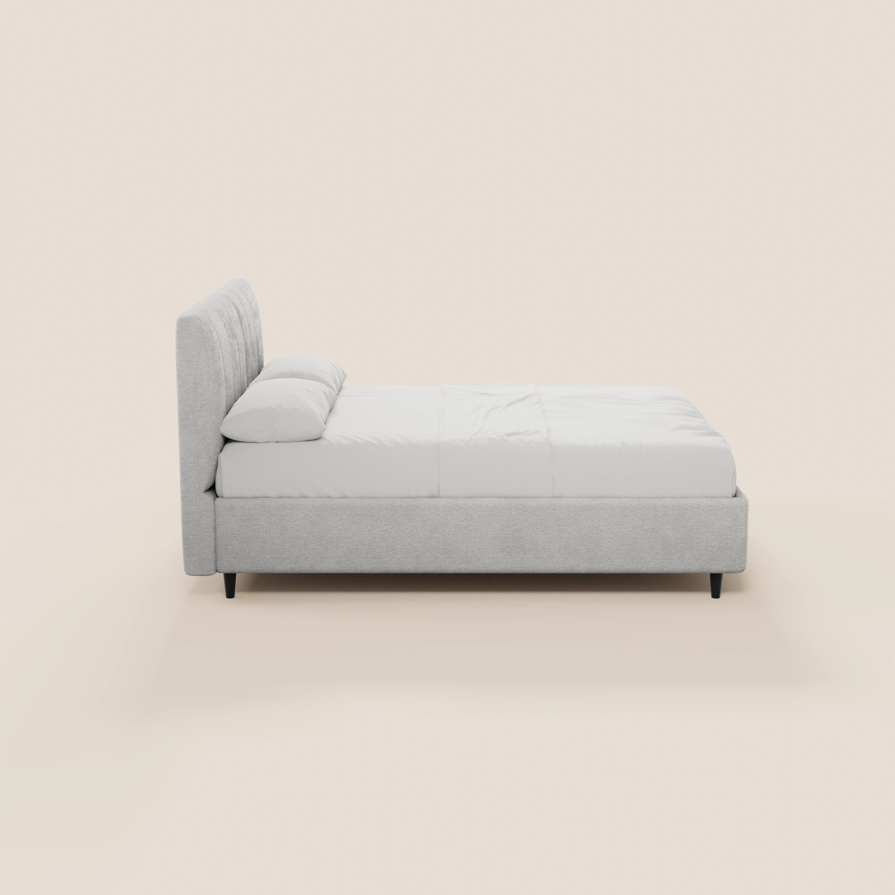 Il letto imbottito ONYX con contenitore di Letti.store presenta una struttura imbottita dal profilo ribassato, di colore grigio chiaro e certificata Oeko-Tex®, una testiera verticale, biancheria da letto bianca, due cuscini e gambe corte nere; nella foto è raffigurato di profilo su uno sfondo beige chiaro.