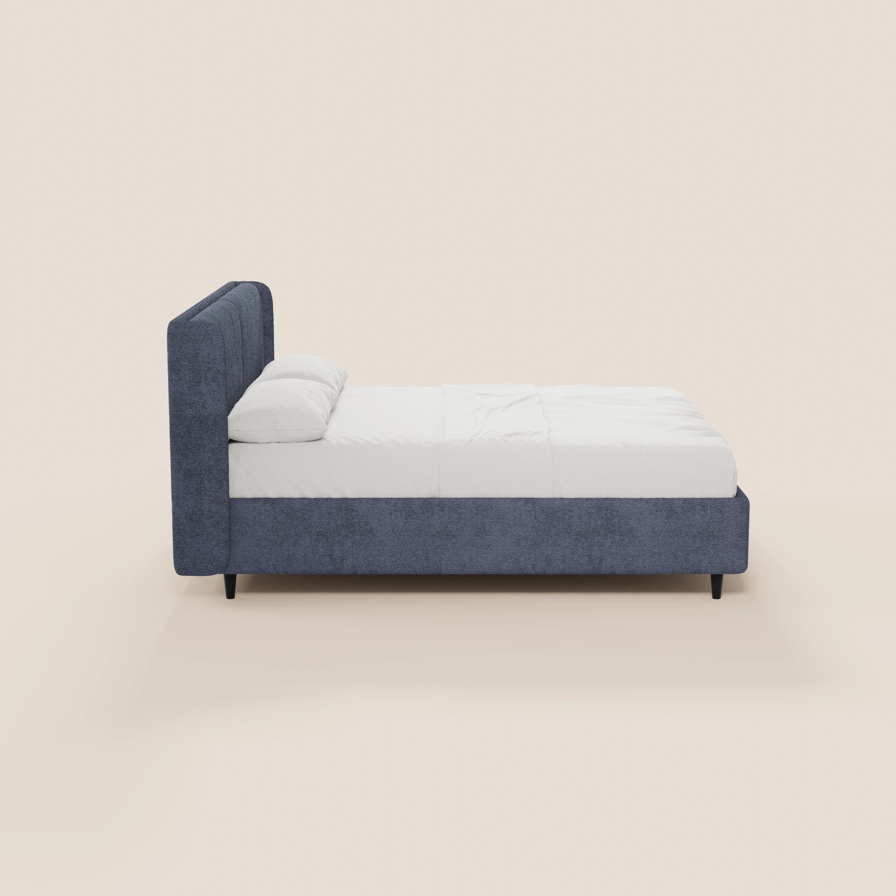 Una vista laterale del letto di design VALKIRIA di Letti.store, caratterizzato da un’alta testiera avvolgente imbottita di colore blu scuro con 2 cuscini imbottiti in tessuto Oeko-Tex®, biancheria da letto bianca e struttura blu abbinata su gambe corte nere, il tutto su uno sfondo beige.