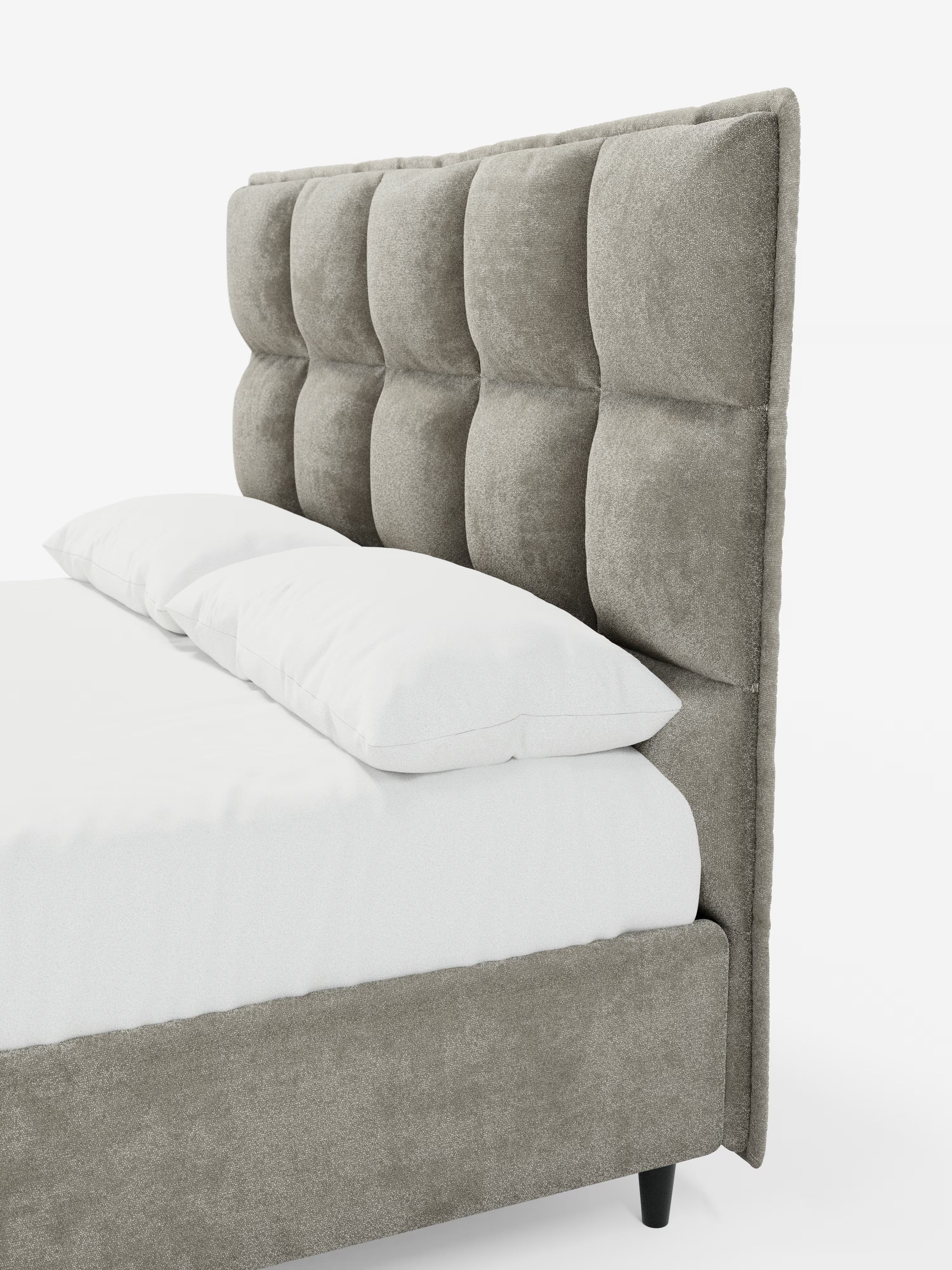 Un primo piano del letto imbottito con contenitore AURO di Letti.store, caratterizzato da una testiera alta e capitonné, rivestita in tessuto ciniglia grigio certificato Oeko-Tex® con ampi pannelli quadrati. Il letto è abbellito da un lenzuolo con angoli bianco e due cuscini bianchi, mentre la struttura imbottita è in tinta con il tessuto della testiera e poggia su corte gambe nere.