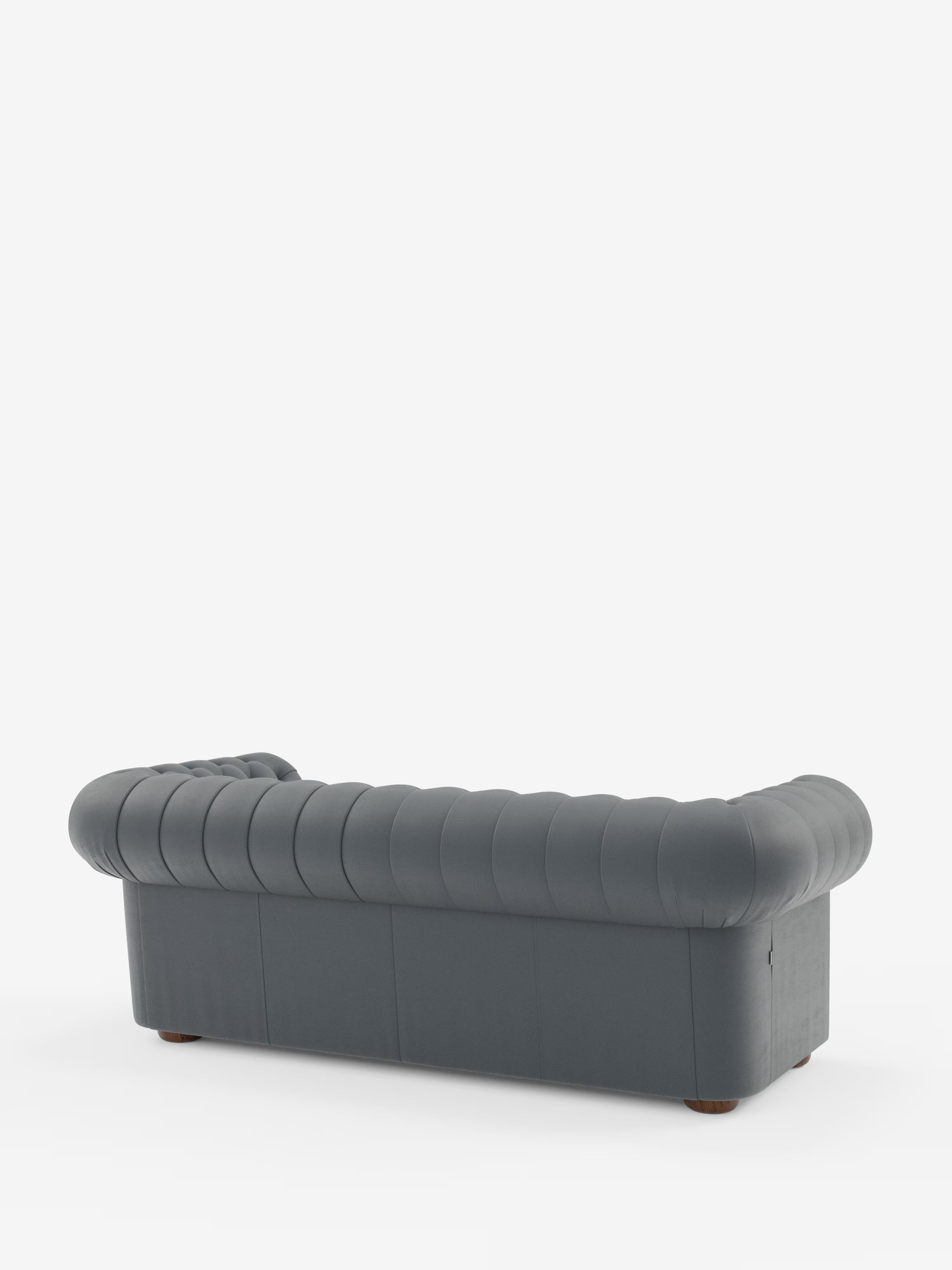 Un Chester grigio scuro – Divano Chesterfield in vera pelle spessorata a 2 e 3 posti di Divani.Store è raffigurato in una vista posteriore obliqua, caratterizzato da un rivestimento in pelle trapuntata con braccioli e schienale arrotondati, e poggiante su piedini corti e rotondi in legno su uno sfondo bianco a tinta unita. Questo elegante divano artigianale Made in Italy coniuga perfettamente uno stile intramontabile con la maestria artigianale.