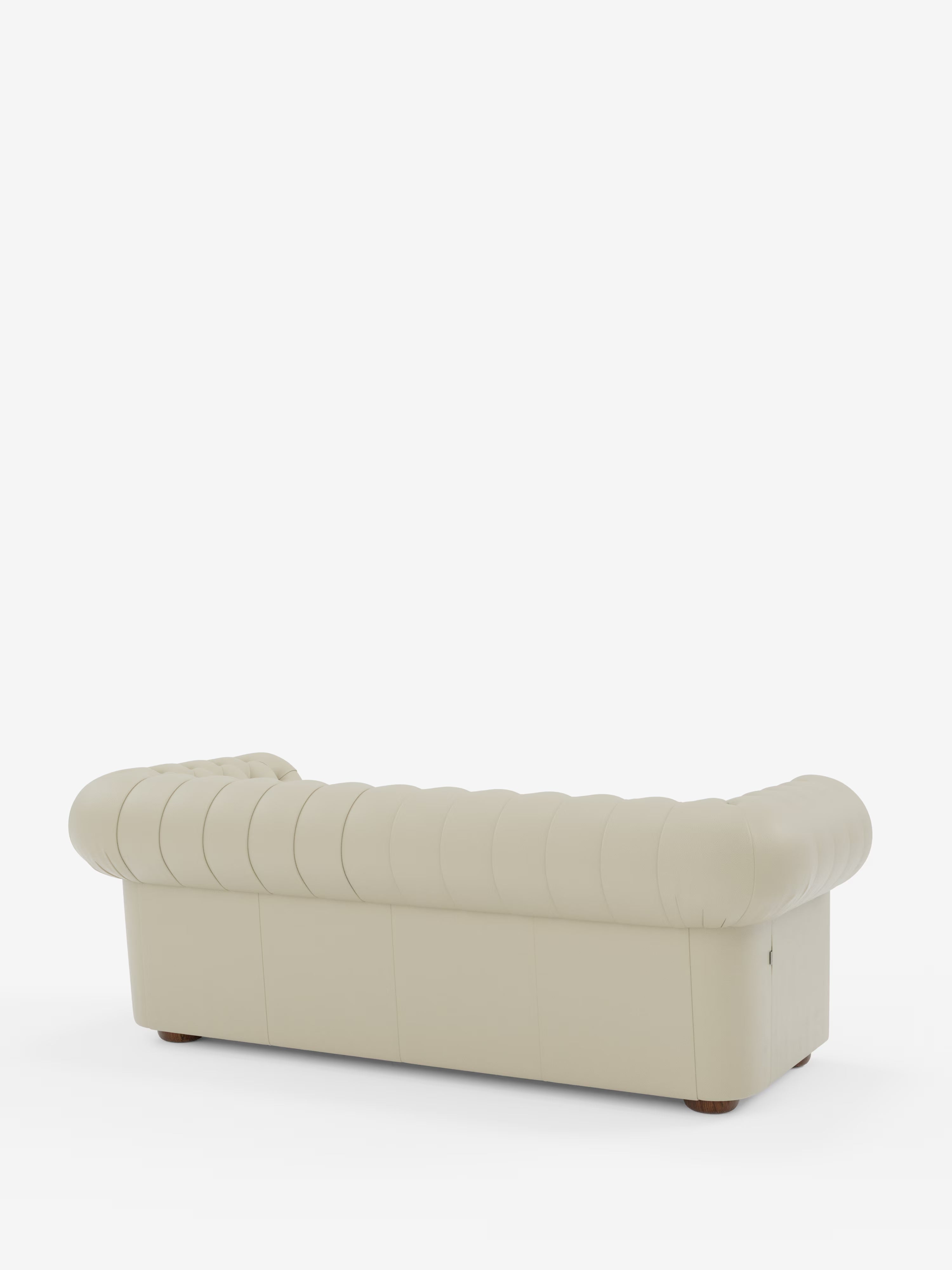 Un divano Chesterfield color crema con capitonné – Divano Chesterfield in vera pelle spessorata a 2 e 3 posti di Divani.Store, con braccioli e schienale arrotondati, ripreso da dietro in una prospettiva obliqua. Questo elegante divano artigianale Made in Italy presenta piccole gambe circolari in legno ed è posizionato su uno sfondo bianco a tinta unita.