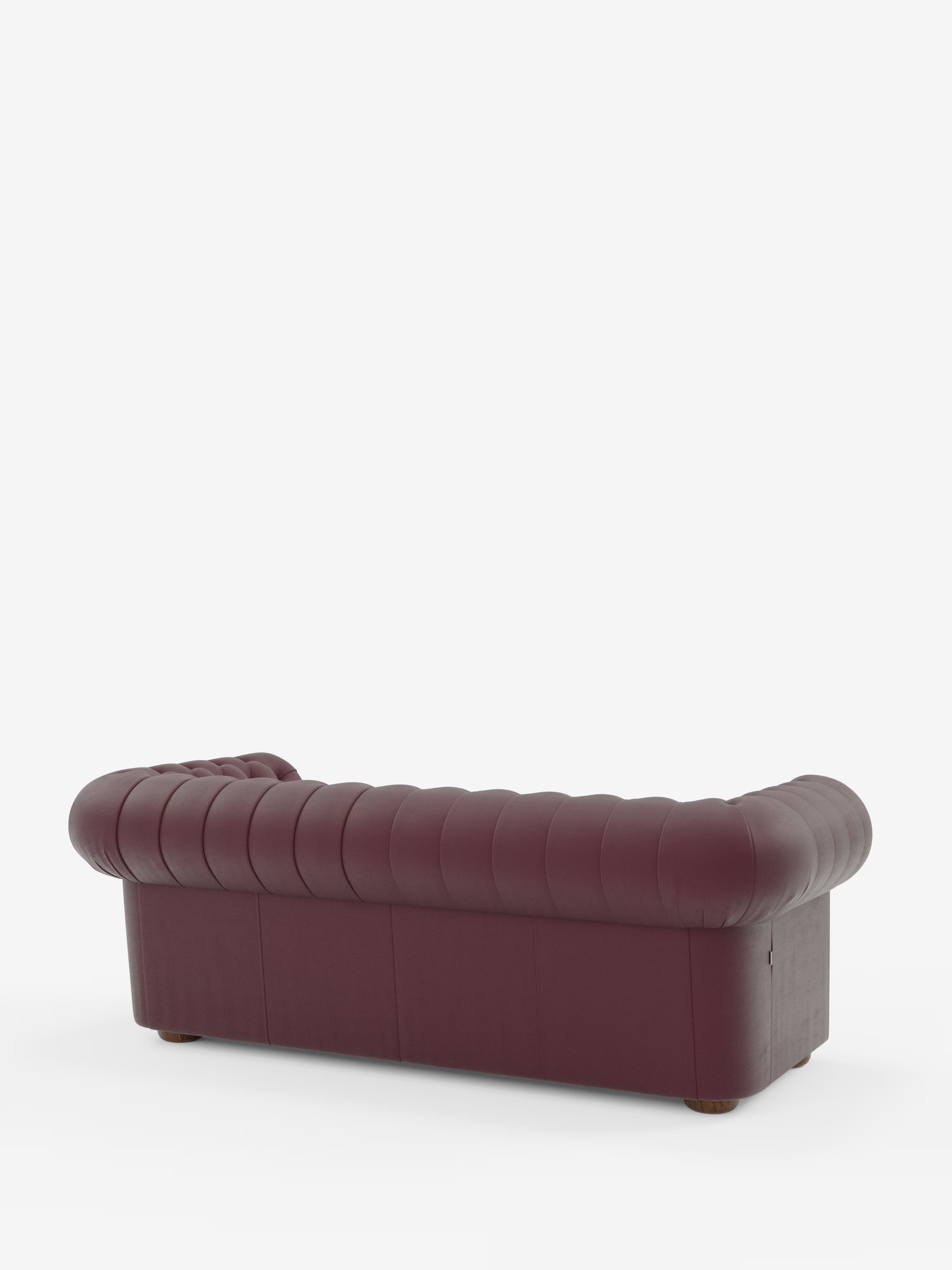 Un divano Chesterfield in pelle marrone rossiccio — il modello Chester di Divani.Store, un divano Chesterfield in vera pelle spessorata disponibile nella versione a 2 o 3 posti — è ripreso di profilo dal retro su uno sfondo bianco a tinta unita. Questo elegante divano presenta una profonda trapuntatura e braccioli arrotondati, con gambe corte in legno che ne accentuano il design intramontabile e la qualità artigianale di Divani.Store.