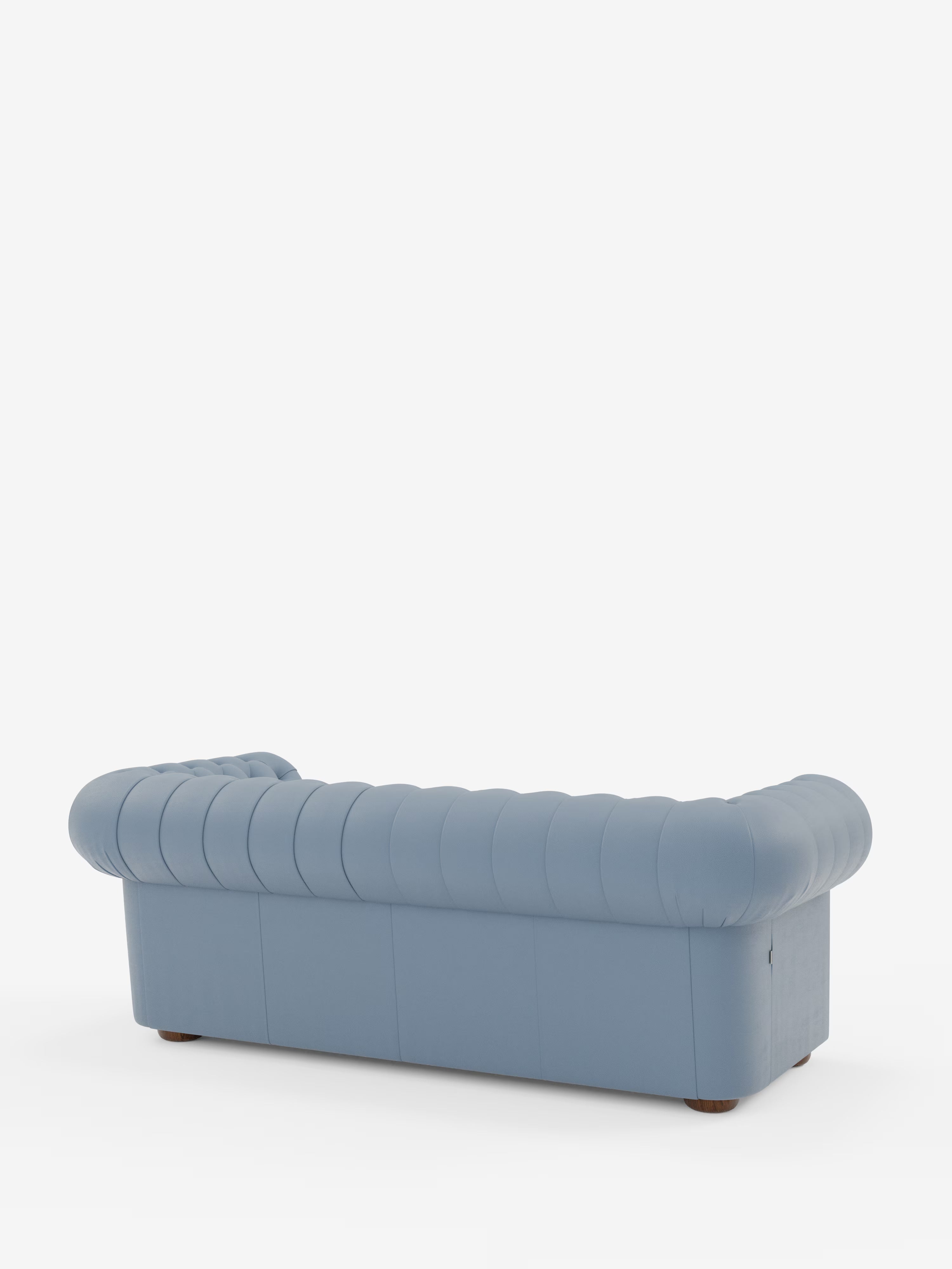 Un divano Chesterfield azzurro, imbottito – Divano Chesterfield in vera pelle spessorata a 2 e 3 posti di Divani.Store – è ripreso di profilo, visto da dietro. Questo elegante divano artigianale italiano presenta braccioli profondi e arrotondati e uno schienale con dettagli trapuntati verticali. Lo sfondo è bianco a tinta unita.