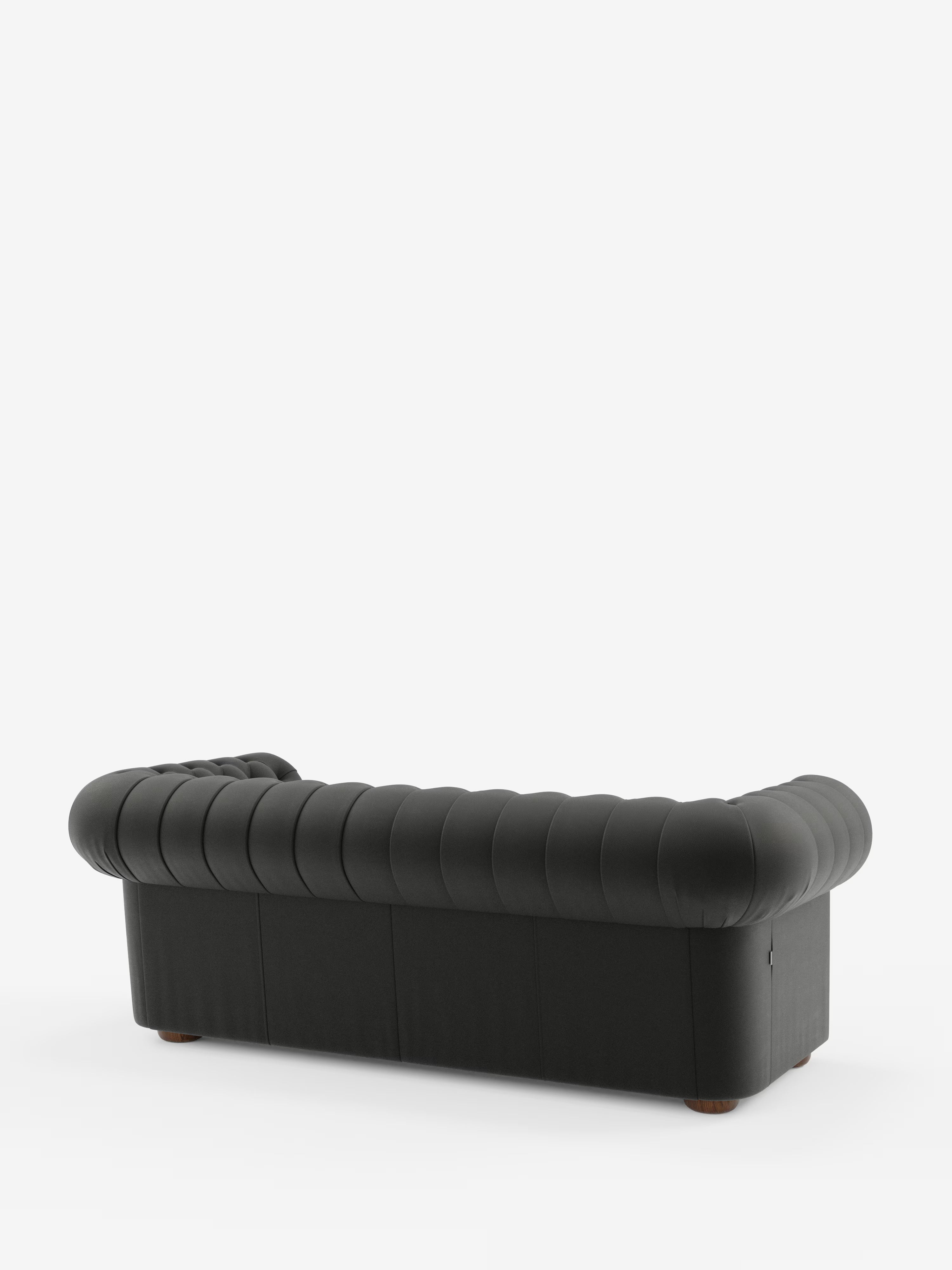 Un Chester nero – Divano Chesterfield in vera pelle spessorata di Divani.Store è ripreso di retro su uno sfondo bianco a tinta unita; presenta braccioli e schienale arrotondati con sottili cuciture verticali e gambe corte e arrotondate in legno scuro: un raffinato esempio di artigianato italiano.