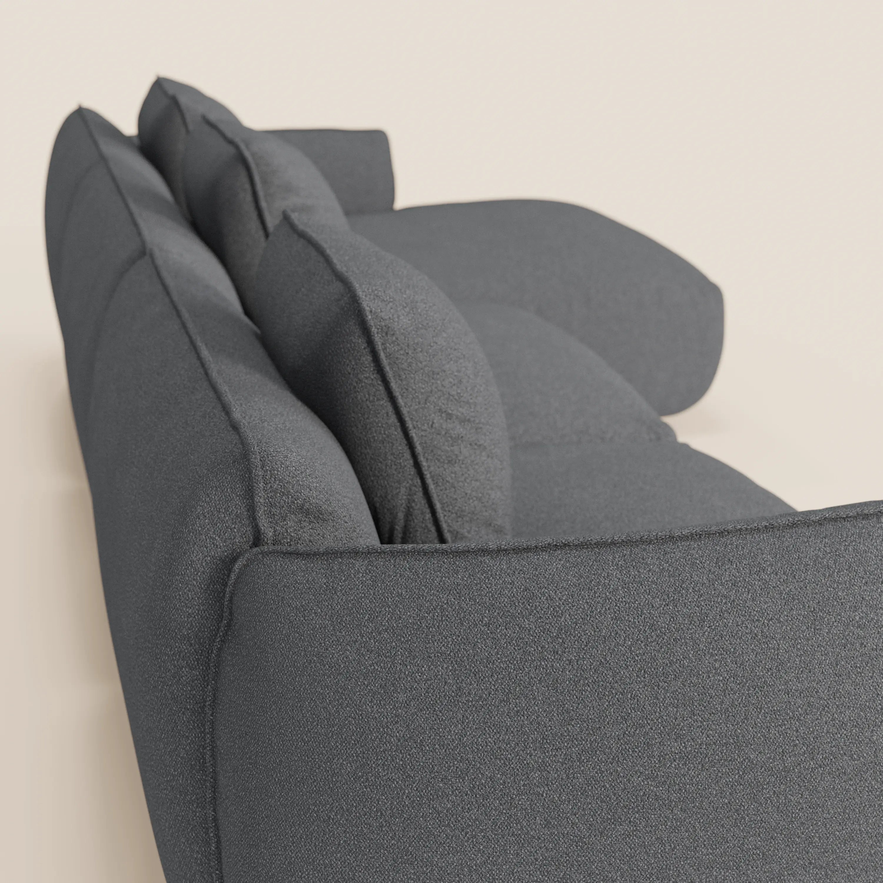 Una vista angolare ravvicinata del divano angolare Nimbus con penisola componibile di Divani.Store, con tessuto morbido effetto cotone smacchiabile T33 in grigio scuro, mette in evidenza i suoi cuscini morbidi, gli ampi braccioli e il comfort invitante su uno sfondo semplice.