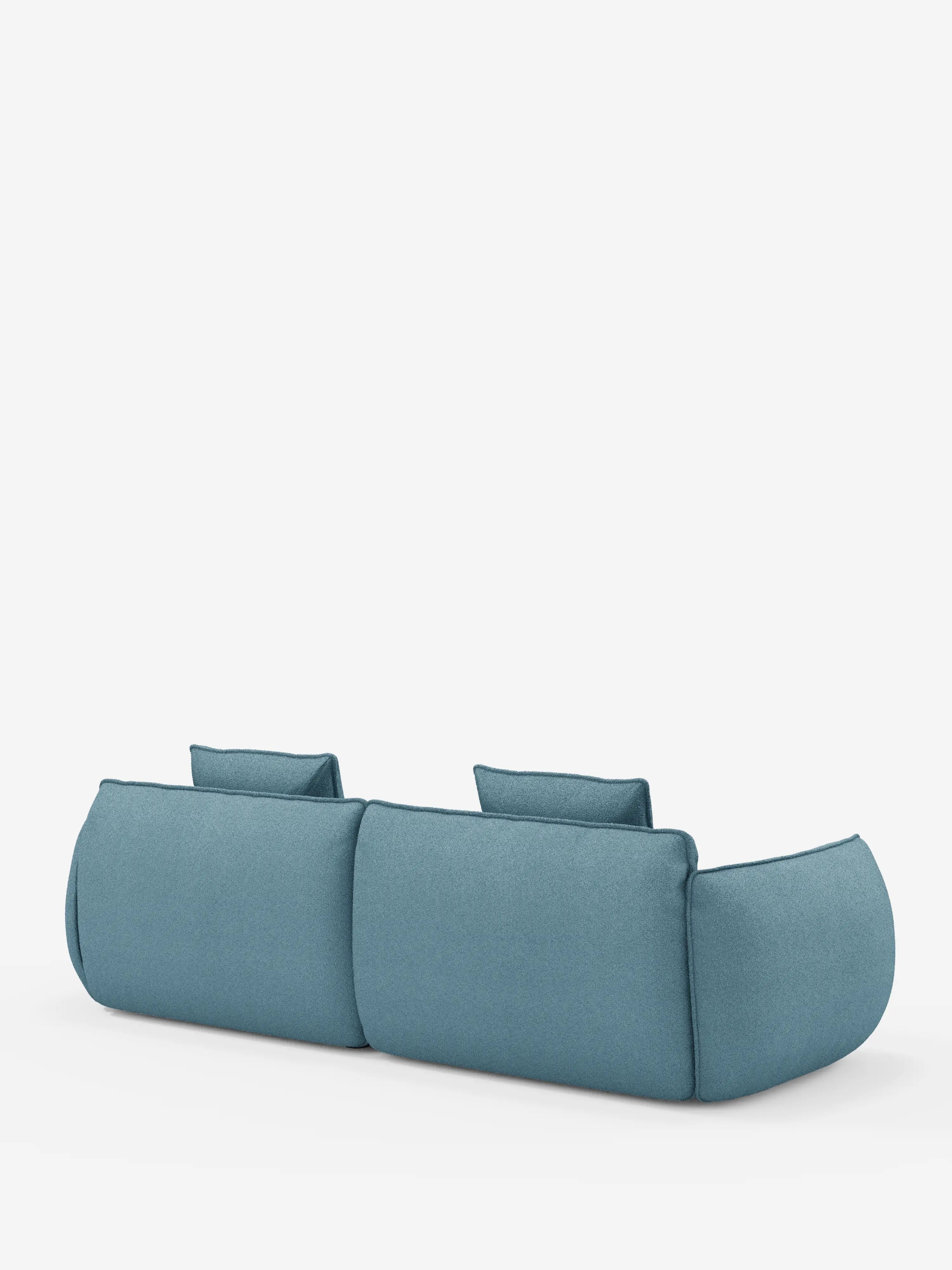 Il divano Nimbus, un modello moderno e minimalista a 3 posti, modulare e componibile di Divani.Store, lungo 250 cm, è raffigurato di retro in una tonalità di blu tenue, rivestito in tessuto smacchiabile effetto cotone T33. Il design presenta bordi arrotondati, braccioli bassi, cuscini morbidi e due poggiatesta. Lo sfondo è bianco a tinta unita.