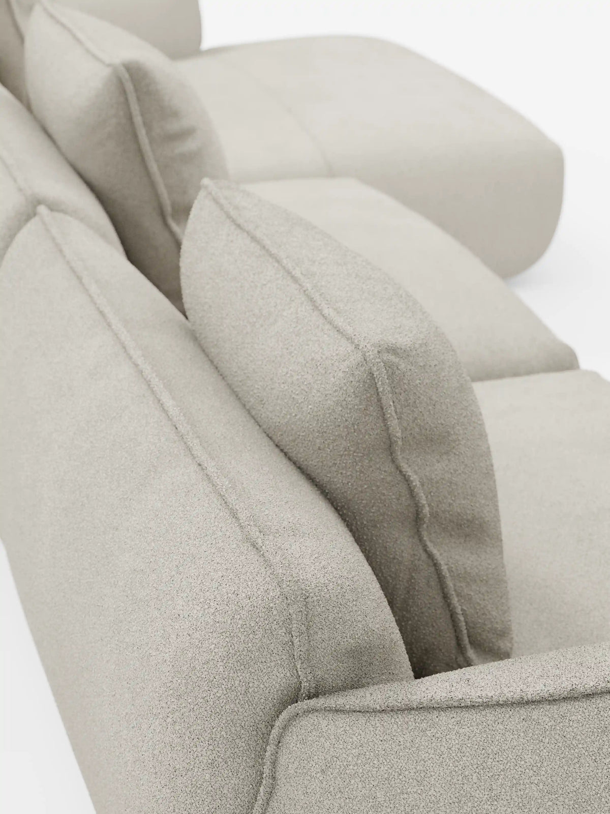 Primo piano del divano angolare con penisola componibile Nimbus di Divani.Store, rivestito in morbido tessuto effetto cotone T33, resistente alle macchie, in una tonalità beige chiaro. L'immagine è ripresa da dietro e leggermente dall'alto, mettendo in risalto i cuscini morbidi e testurizzati e mostrando l'allineamento dello schienale e della seduta su uno sfondo bianco.