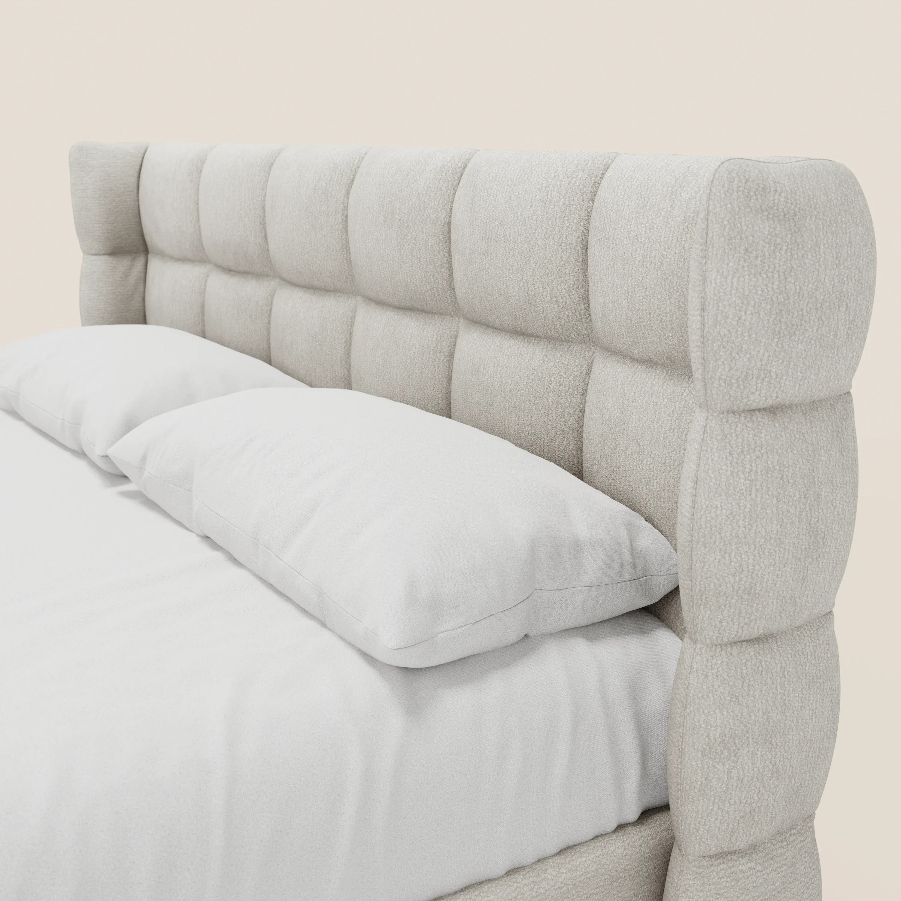 Primo piano del letto imbottito RAGNAR con contenitore e testiera capitonné avvolgente in elegante tessuto Oeko-Tex® di Letti.store, raffigurato in beige chiaro con cuscini e biancheria da letto bianchi su uno sfondo neutro.