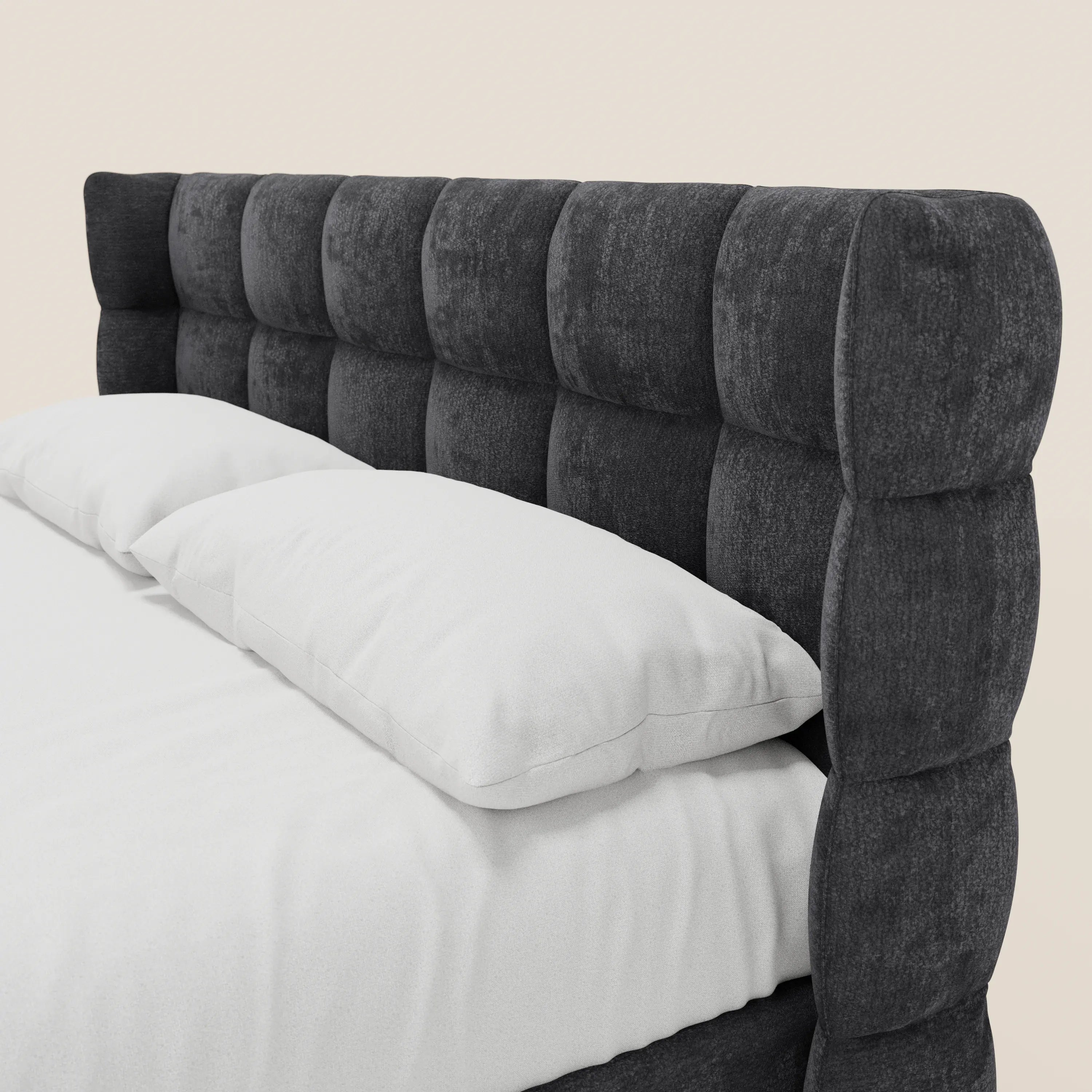 Un primo piano del letto imbottito RAGNAR con contenitore di Letti.store, con testiera capitonné avvolgente in elegante tessuto Oeko-Tex®, in grigio scuro con motivo a griglia, con biancheria bianca e due cuscini, su sfondo beige chiaro.