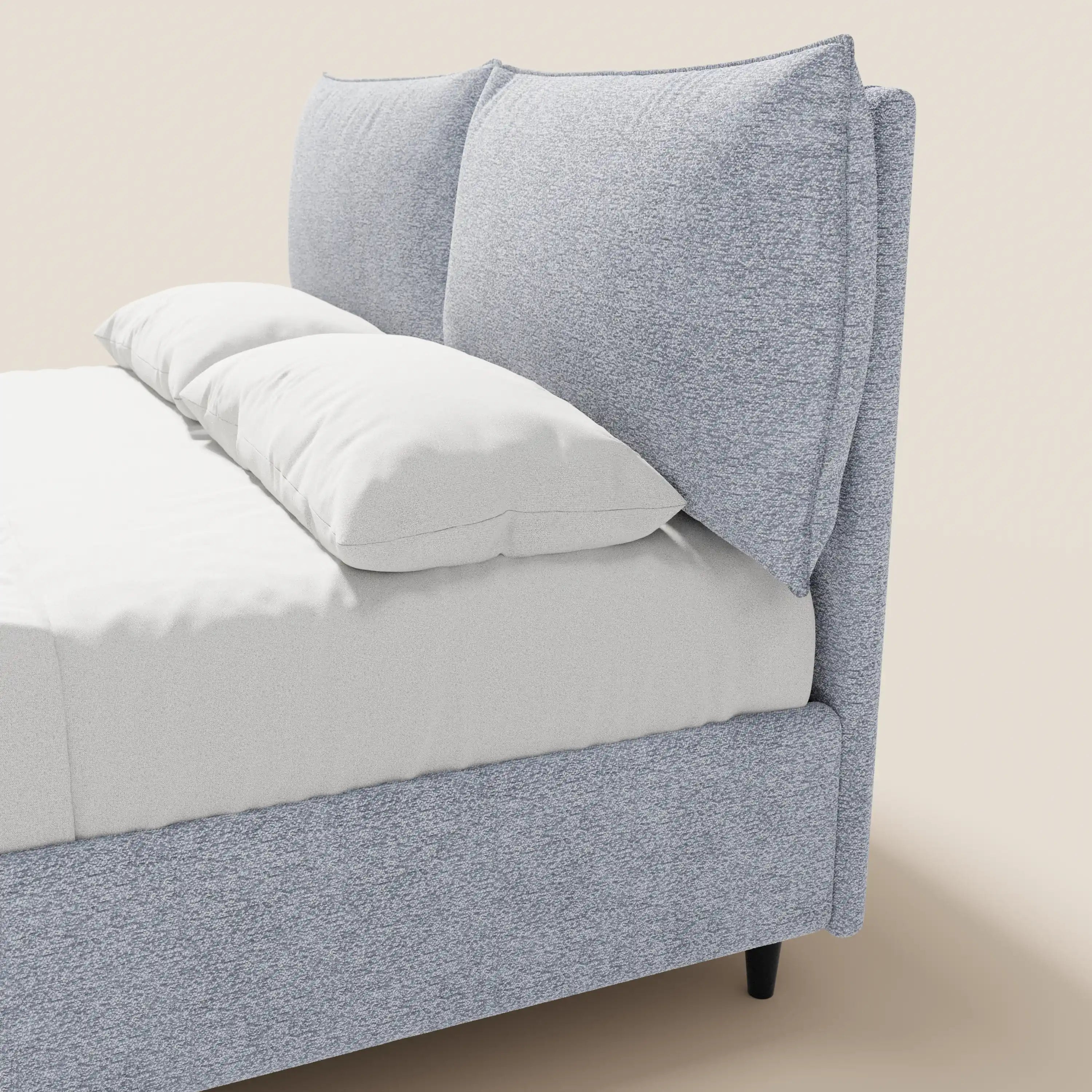 Un primo piano del letto imbottito ZAYRON di Letti.store, caratterizzato da una moderna struttura in tessuto grigio chiaro certificato Oeko-Tex®, cuscini morbidi regolabili e un vano portaoggetti. Su uno sfondo beige, è visibile solo una parte del letto con lenzuola bianche.