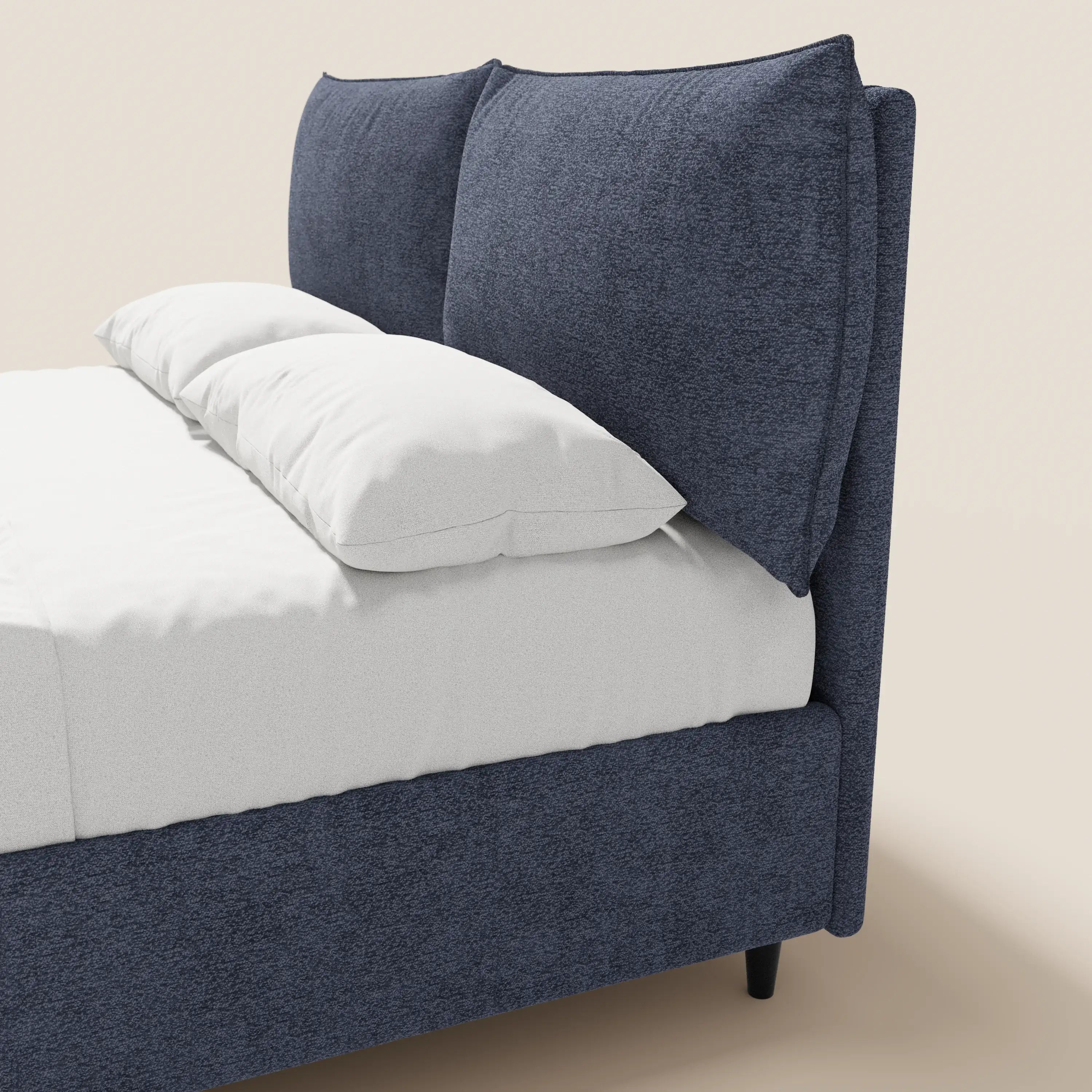 Il letto imbottito ZAYRON di Letti.store, con contenitore e morbidi cuscini regolabili in tessuto blu navy Oeko-Tex®, è raffigurato parzialmente su uno sfondo beige chiaro, rifinito con lenzuola e cuscini bianchi.
