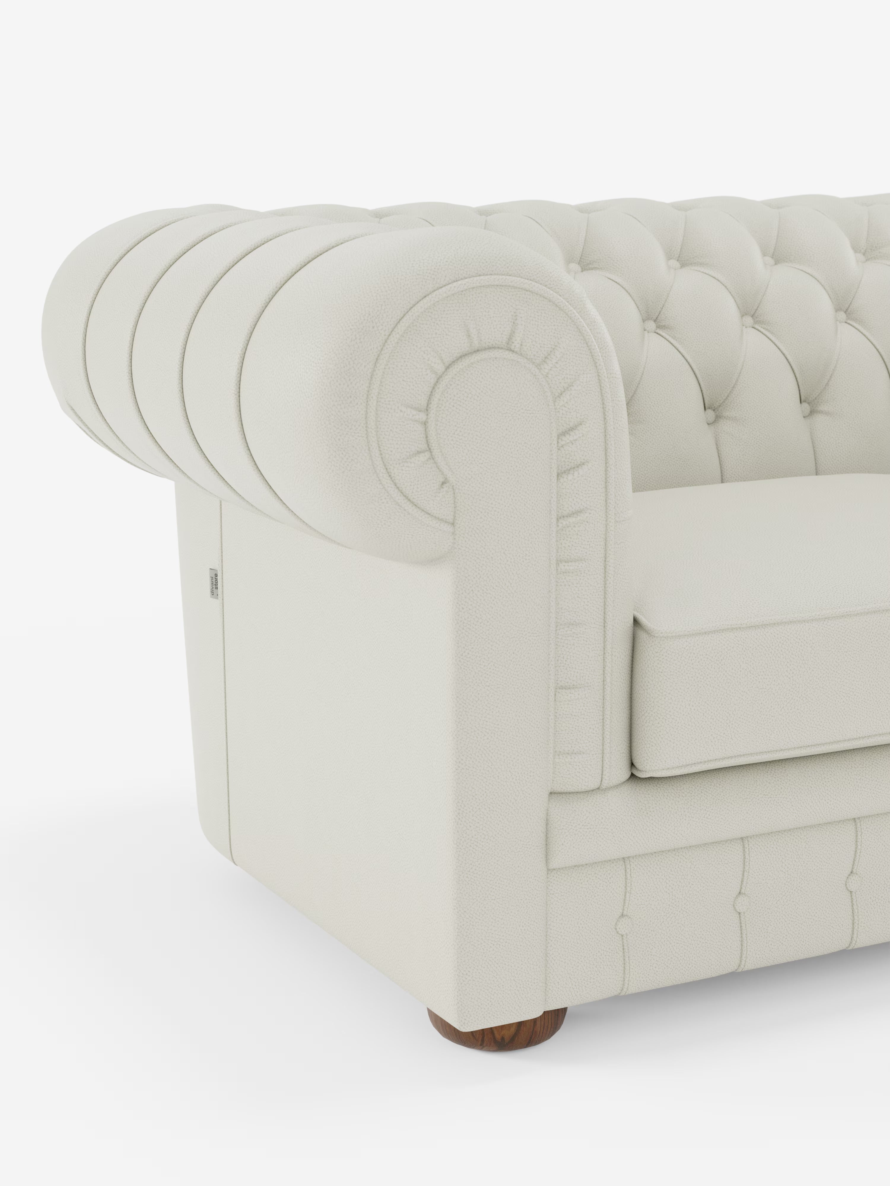 Primo piano del bracciolo sinistro e del cuscino del modello Chester – Divano Chesterfield in vera pelle spessorata a 2 e 3 posti di Divani.Store, caratterizzato da un rivestimento trapuntato color crema chiaro in vera pelle spessorata, un bracciolo arrotondato, profondi bottoni decorativi e gambe corte in legno, su uno sfondo bianco a tinta unita.