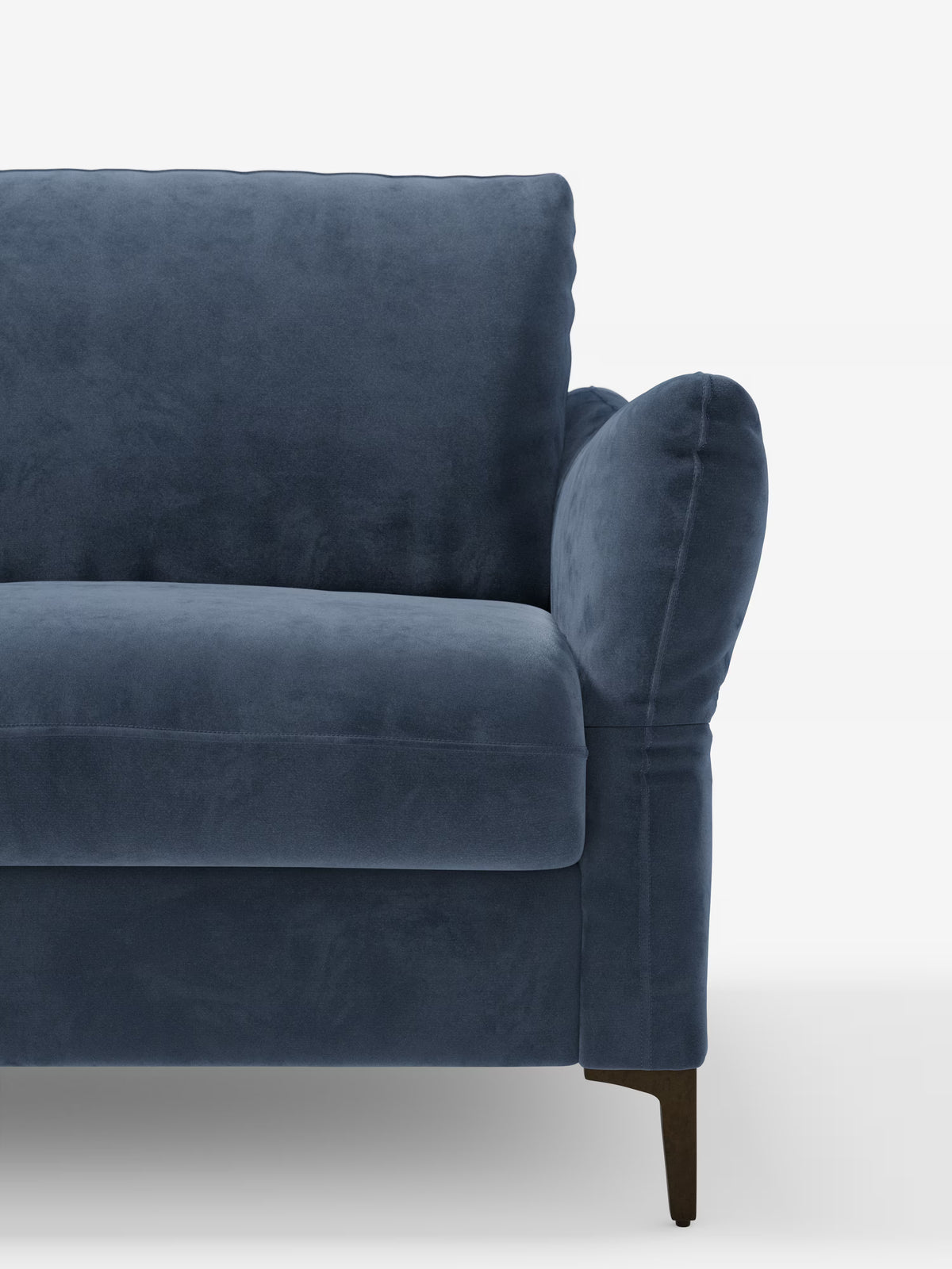 È visibile una parte del divano letto Dalia di Divani.Store, rivestito in un morbido velluto T30 blu scuro resistente alle macchie. Il design moderno di ispirazione scandinava presenta braccioli e schienale dalle linee slanciate e arrotondate, con cuscini di seduta e schienale spessi e confortevoli. La gamba corta in legno del divano è leggermente inclinata. Lo sfondo è bianco a tinta unita.