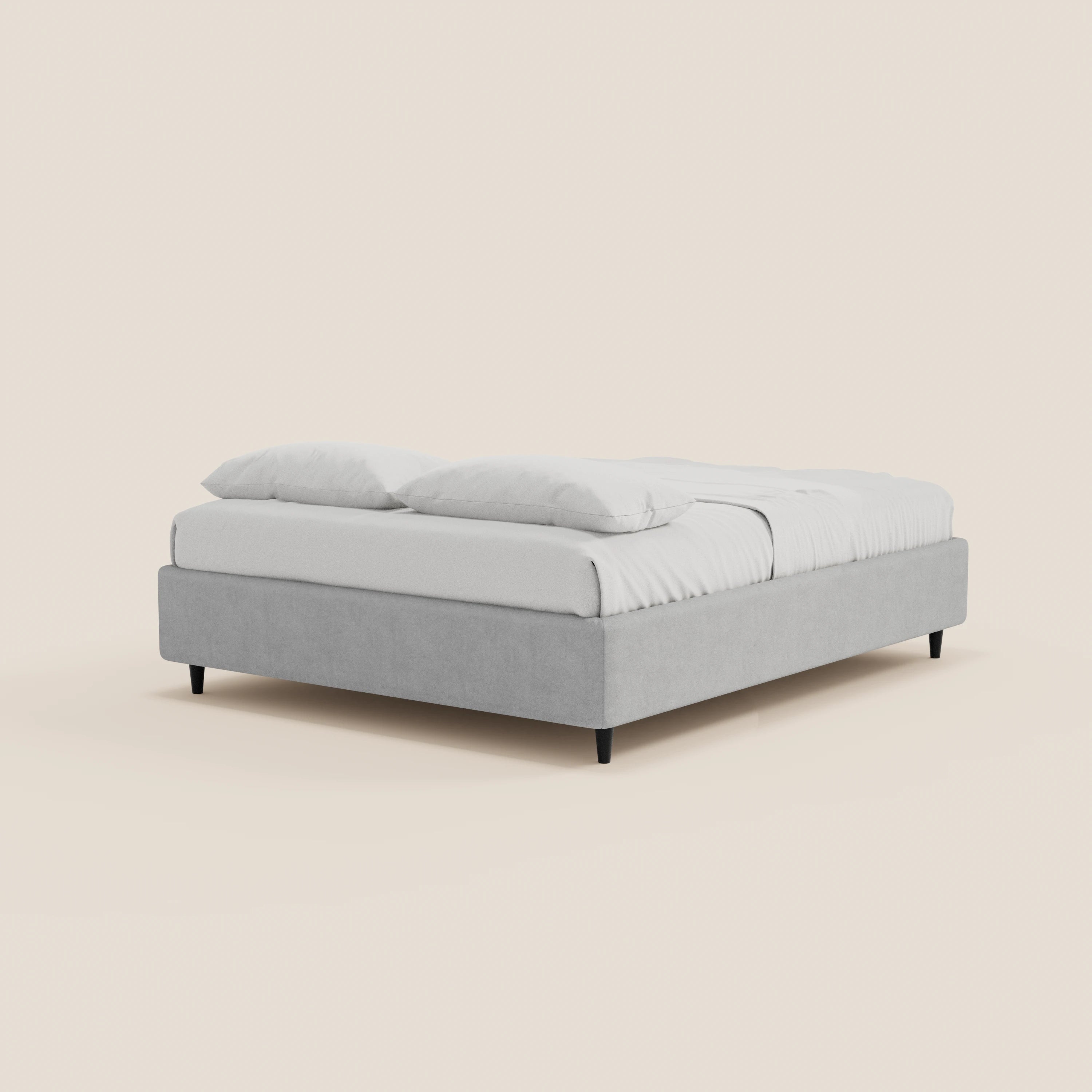 Il letto sommier imbottito ERON con contenitore di Letti.store, realizzato in tessuto impermeabile certificato Oeko-Tex, è disponibile in grigio chiaro con gambe nere, profilo basso e materasso bianco, su sfondo beige chiaro.