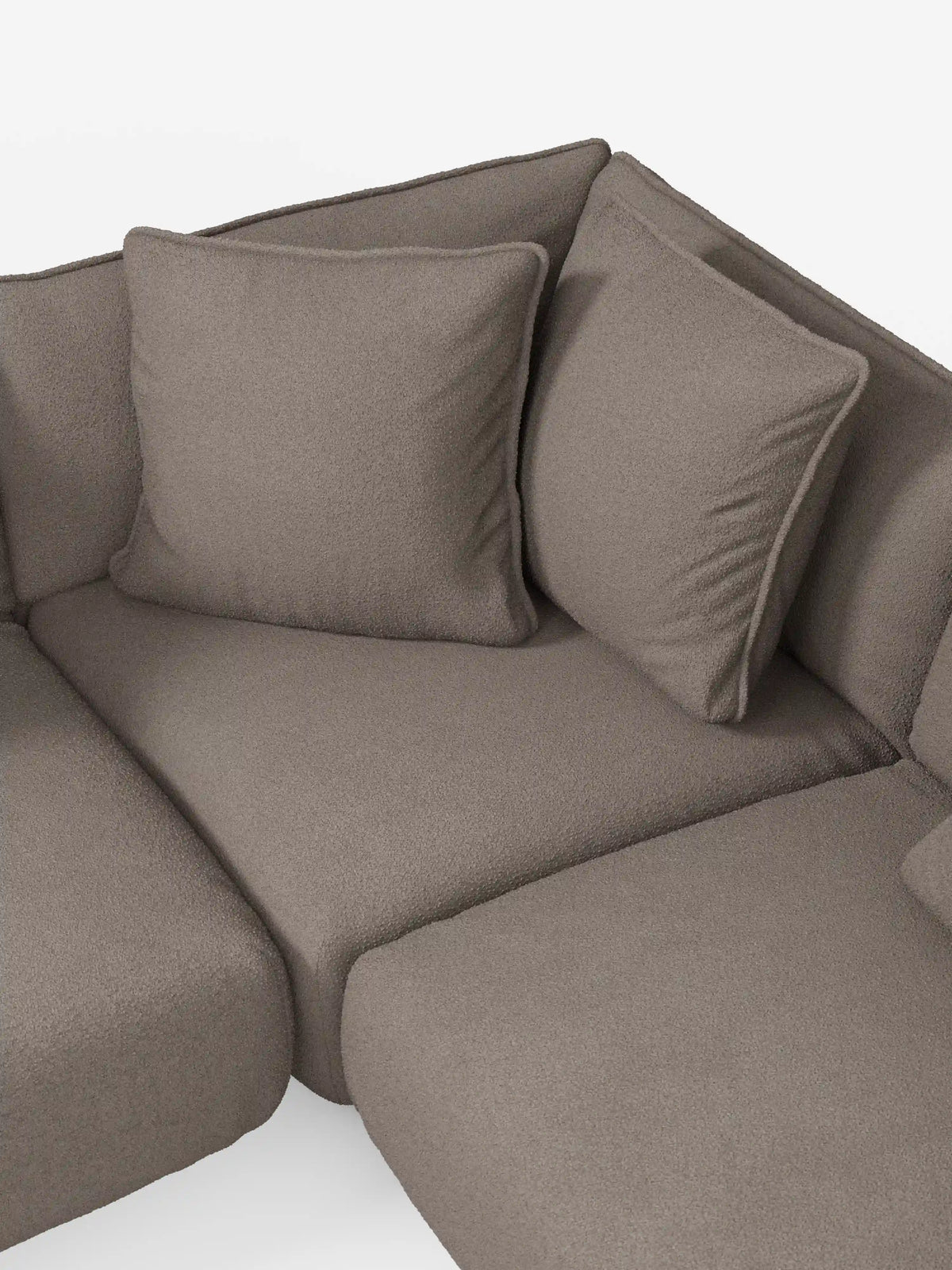 Un primo piano dell'angolo del divano angolare panoramico componibile Nimbus con penisola e angolo in tessuto antimacchia T33 di Divani.Store, caratterizzato da un morbido rivestimento in tessuto color taupe antimacchia e da due cuscini quadrati per lo schienale. Questo divano componibile Made in Italy si distingue per le linee pulite e arrotondate e l’aspetto confortevole, che risalta sullo sfondo bianco chiaro e uniforme.