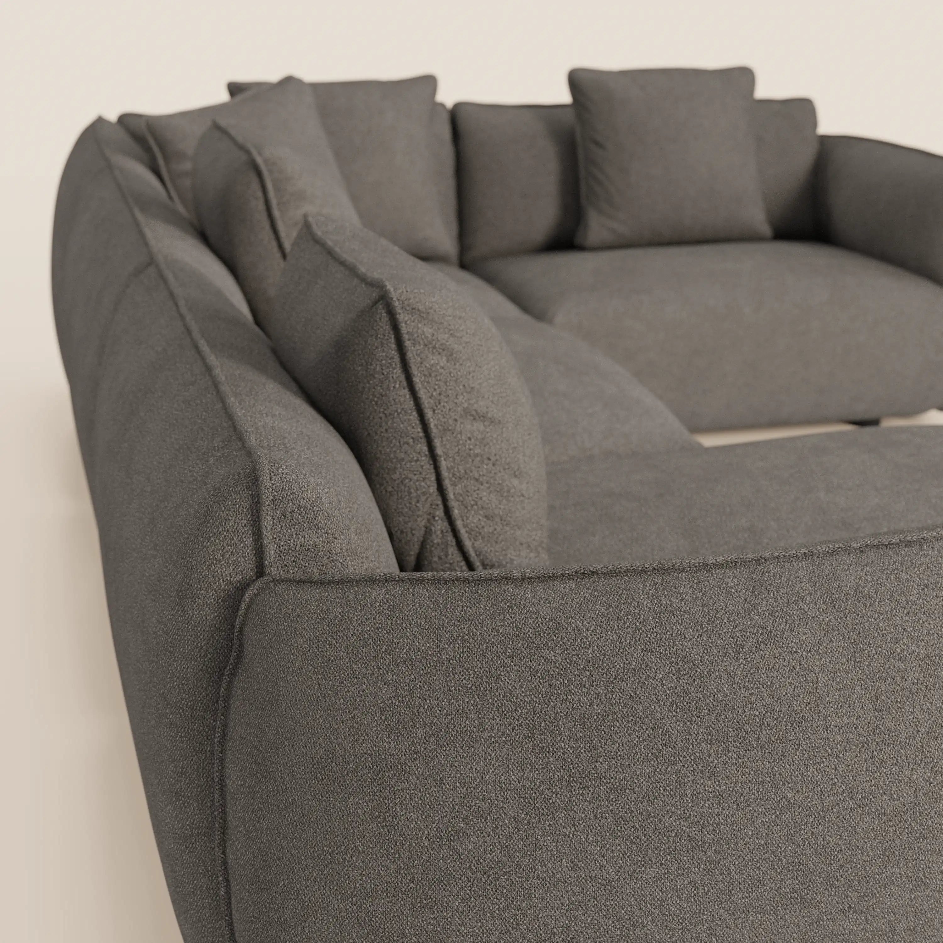 Primo piano di Divani.Store Nimbus divano angolare panoramico componibile con penisola e angolo, rivestito in tessuto antimacchia grigio scuro t33, con spessi braccioli imbottiti e cuscini quadrati coordinati. Fondo beige chiaro a tinta unita.
