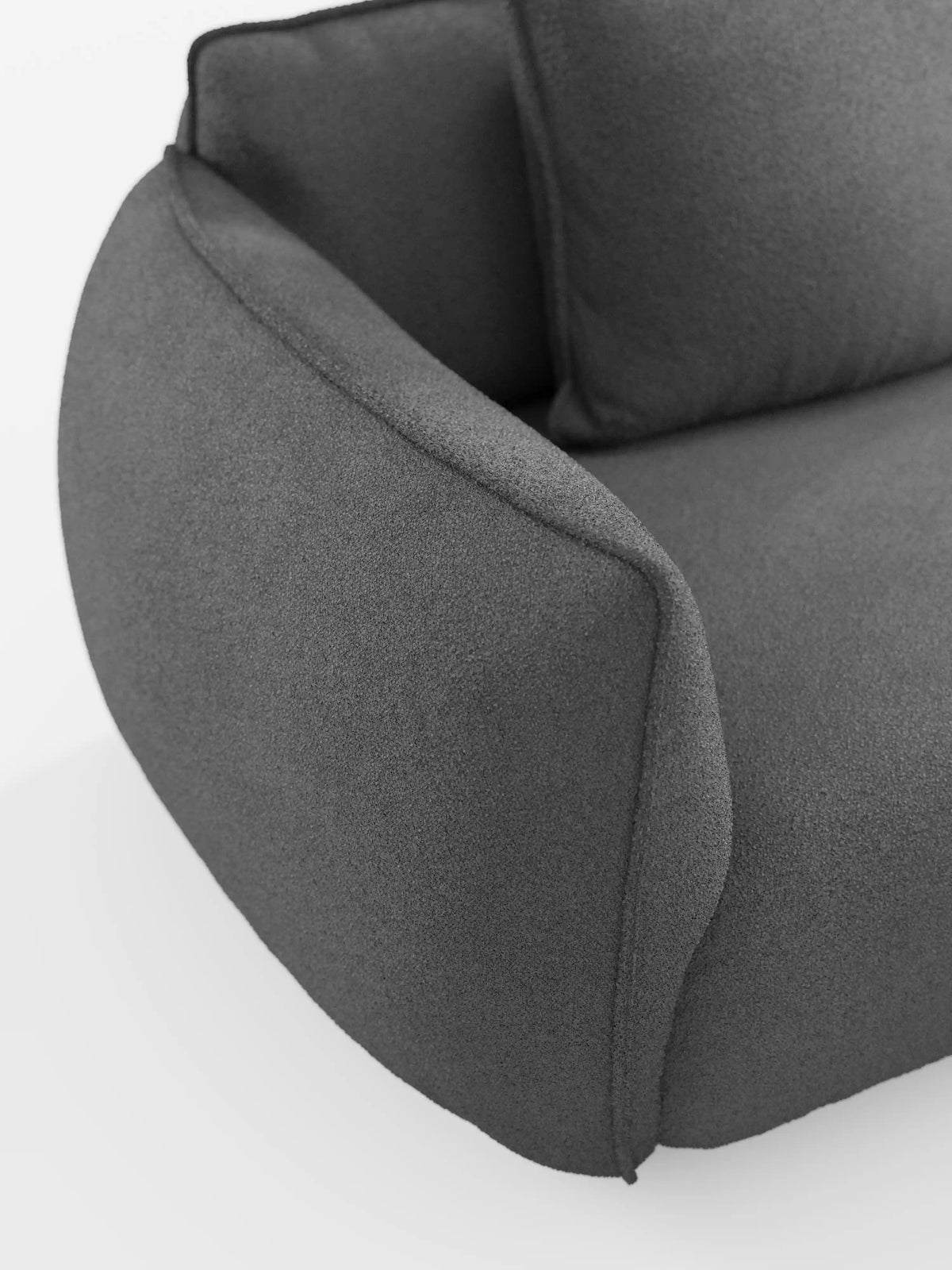 Un primo piano del divano modulare e componibile a 3 posti Nimbus da 250 cm di Divani.Store, rivestito in tessuto T33 effetto cotone lavabile di colore grigio scuro. Il divano modulare presenta un'imbottitura morbida, bordi arrotondati, un bracciolo leggermente rialzato e una texture del tessuto soffice. È ripreso su uno sfondo bianco a tinta unita per mettere in risalto il suo design elegante e minimalista.