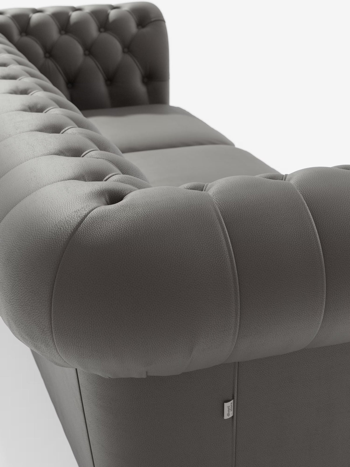 Primo piano del Chester 4 Posti 3 sedute in Vera Pelle – Chesterfield Capitonné Artigianale di Divani.Store: un divano in pelle grigia trapuntata con braccioli spessi e morbidi e profondi bottoni decorativi, che richiamano l’eleganza senza tempo dei classici Chesterfield. Realizzato in vera pelle con cuciture a vista che accentuano lo schienale basso e i braccioli — rifinito con una piccola etichetta in tessuto — questo pezzo Made in Italy è presentato su uno sfondo bianco immacolato, che ne esalta la