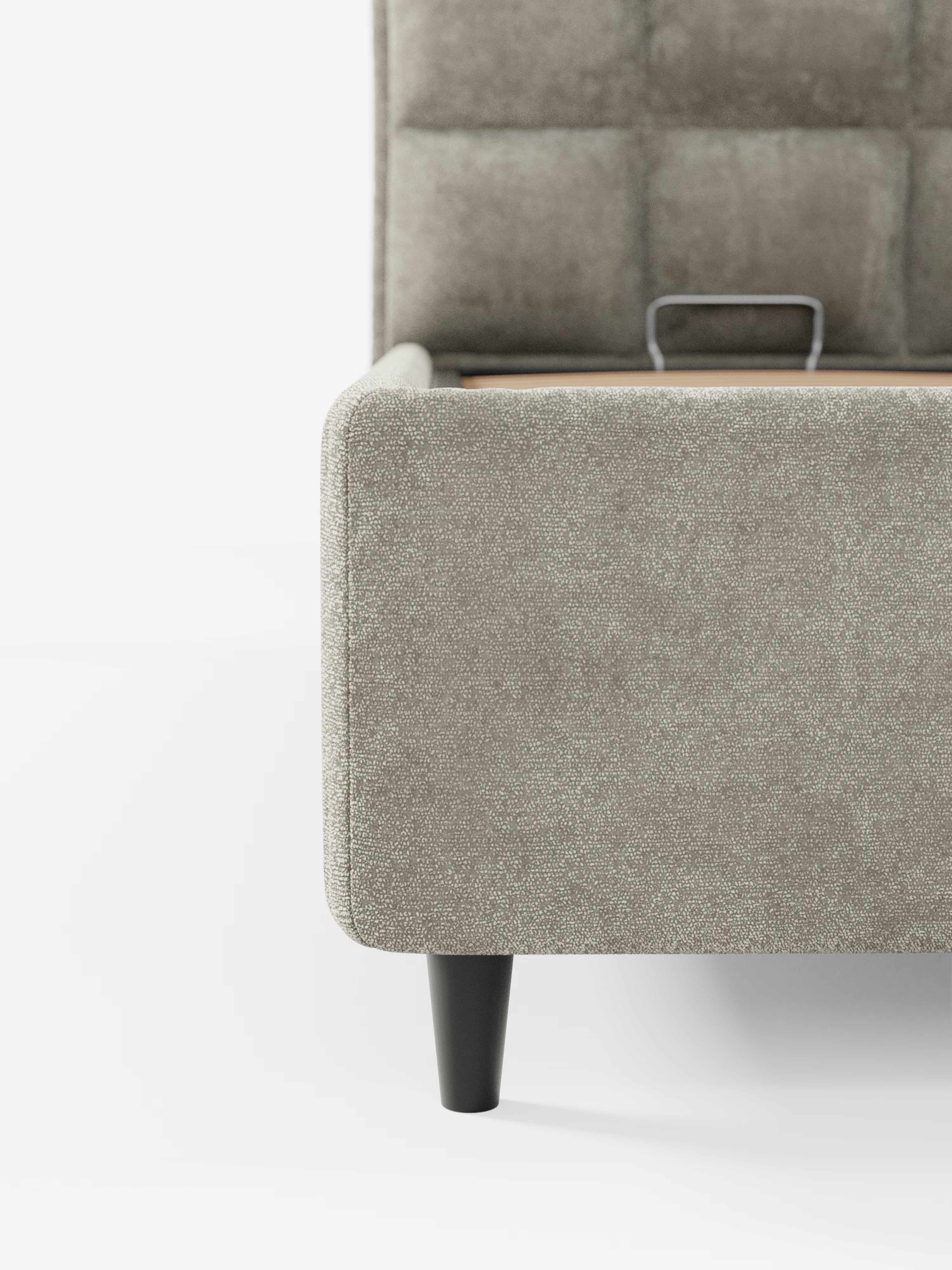 Primo piano dell'angolo del letto imbottito AURO con contenitore e testiera alta capitonné in ciniglia Oeko-Tex® di Letti.store, presentato in grigio chiaro con un morbido rivestimento in ciniglia, gambe corte in legno nero e testiera alta con effetto capitonné; all'interno del telaio è visibile una maniglia in metallo su uno sfondo bianco a tinta unita.