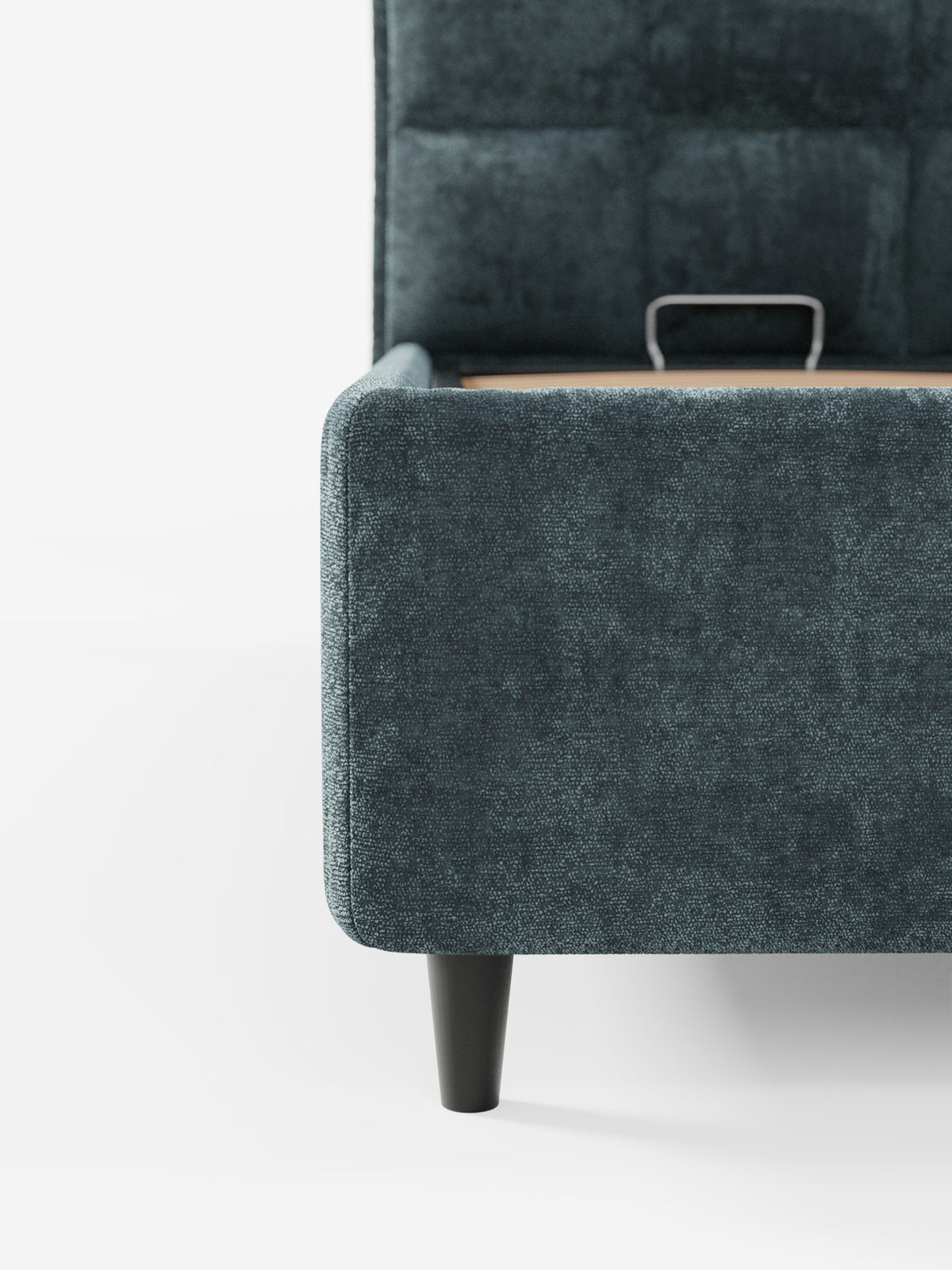 Primo piano di un letto imbottito AURO color verde acqua scuro con contenitore e testiera alta capitonné in ciniglia Oeko-Tex®, modello angolare di Letti.store, caratterizzato da una gamba affusolata nera su sfondo bianco; sono visibili una parte della testiera capitonné alta e un cassetto aperto con maniglia in metallo.
