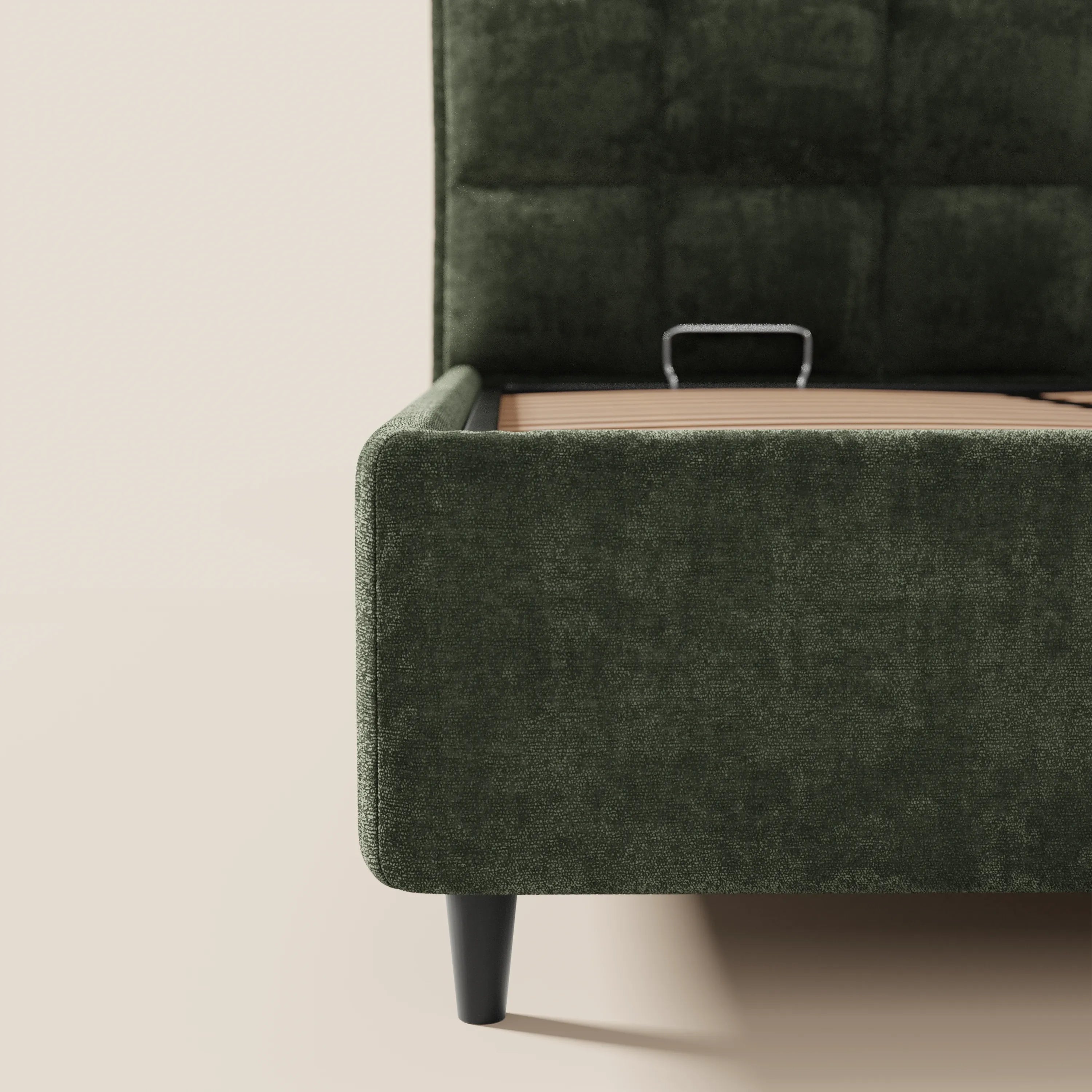 Un primo piano del letto imbottito AURO con contenitore e testiera alta capitonné in ciniglia Oeko-Tex® di Letti.store, caratterizzato da gambe angolate nere e robuste doghe di sostegno in legno, raffigurato su pavimento e pareti chiari.