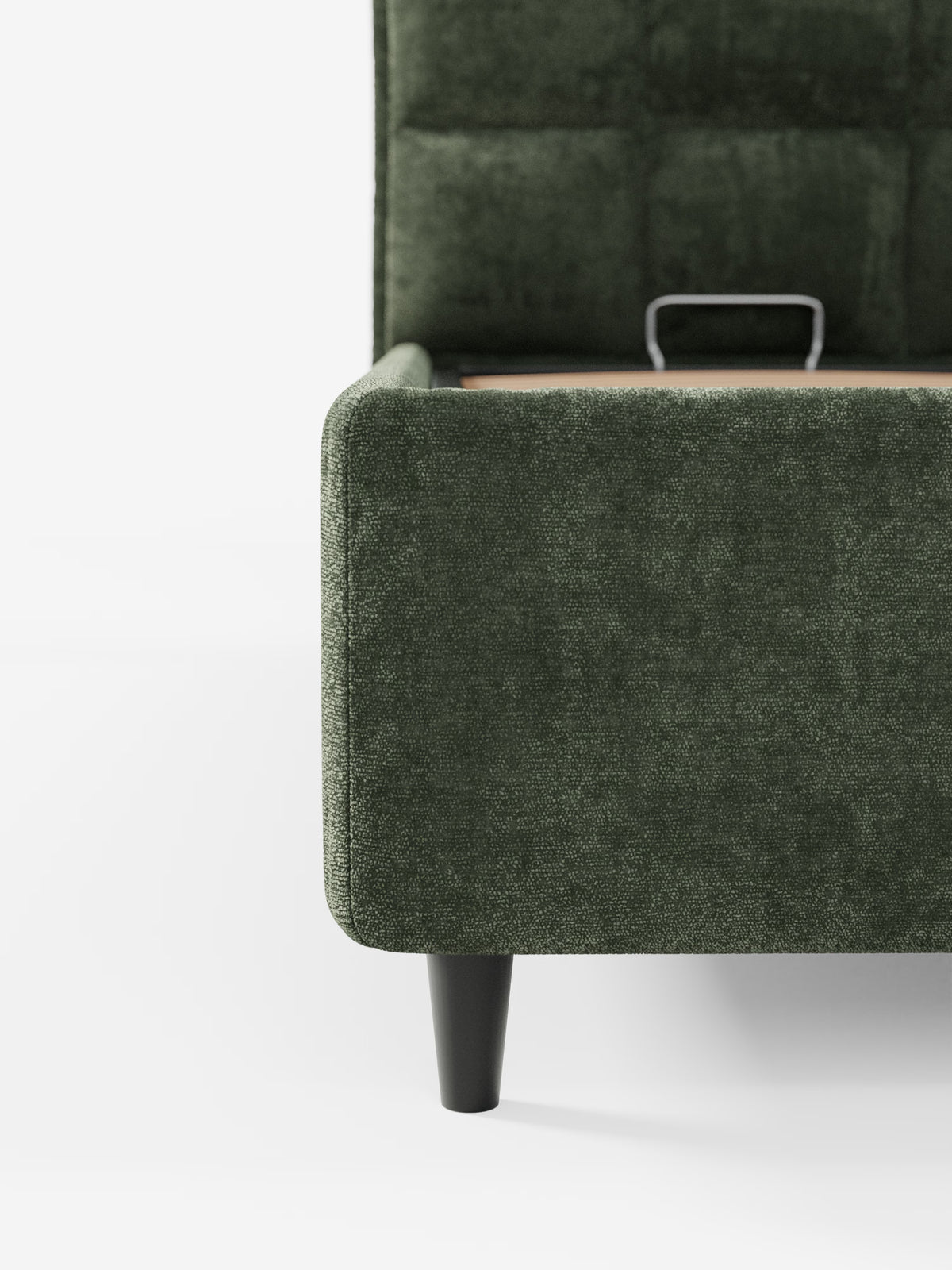 Primo piano del letto imbottito AURO con contenitore e testiera alta capitonné in ciniglia Oeko-Tex® di Letti.store, caratterizzato da un rivestimento verde con texture. L'immagine mette in risalto l'angolo di questo letto personalizzabile, mostrando una gamba affusolata nera e una piccola maniglia in metallo sul lato, su uno sfondo bianco. È visibile solo una parte del letto.
