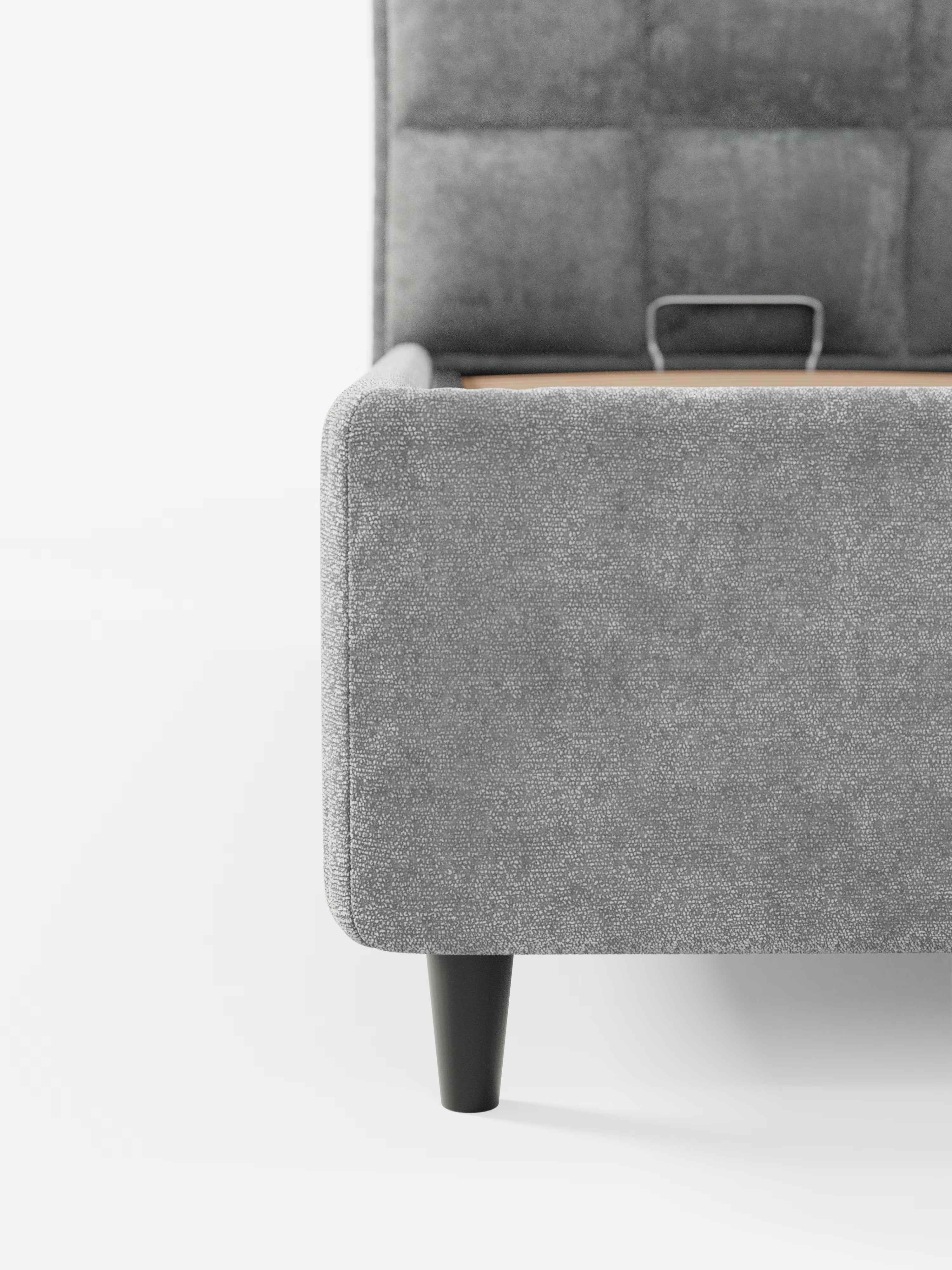 Un primo piano della base del letto imbottito AURO con vano contenitore e testiera capitonné alta in ciniglia Oeko-Tex® di Letti.store mette in risalto il rivestimento in ciniglia grigia che conferisce un aspetto morbido e ricco di texture. Le gambe angolate nere aggiungono un tocco di modernità, mentre la testiera alta presenta un motivo trapuntato a griglia: un’interpretazione contemporanea del classico stile capitonné. Lo sfondo è bianco a tinta unita.
