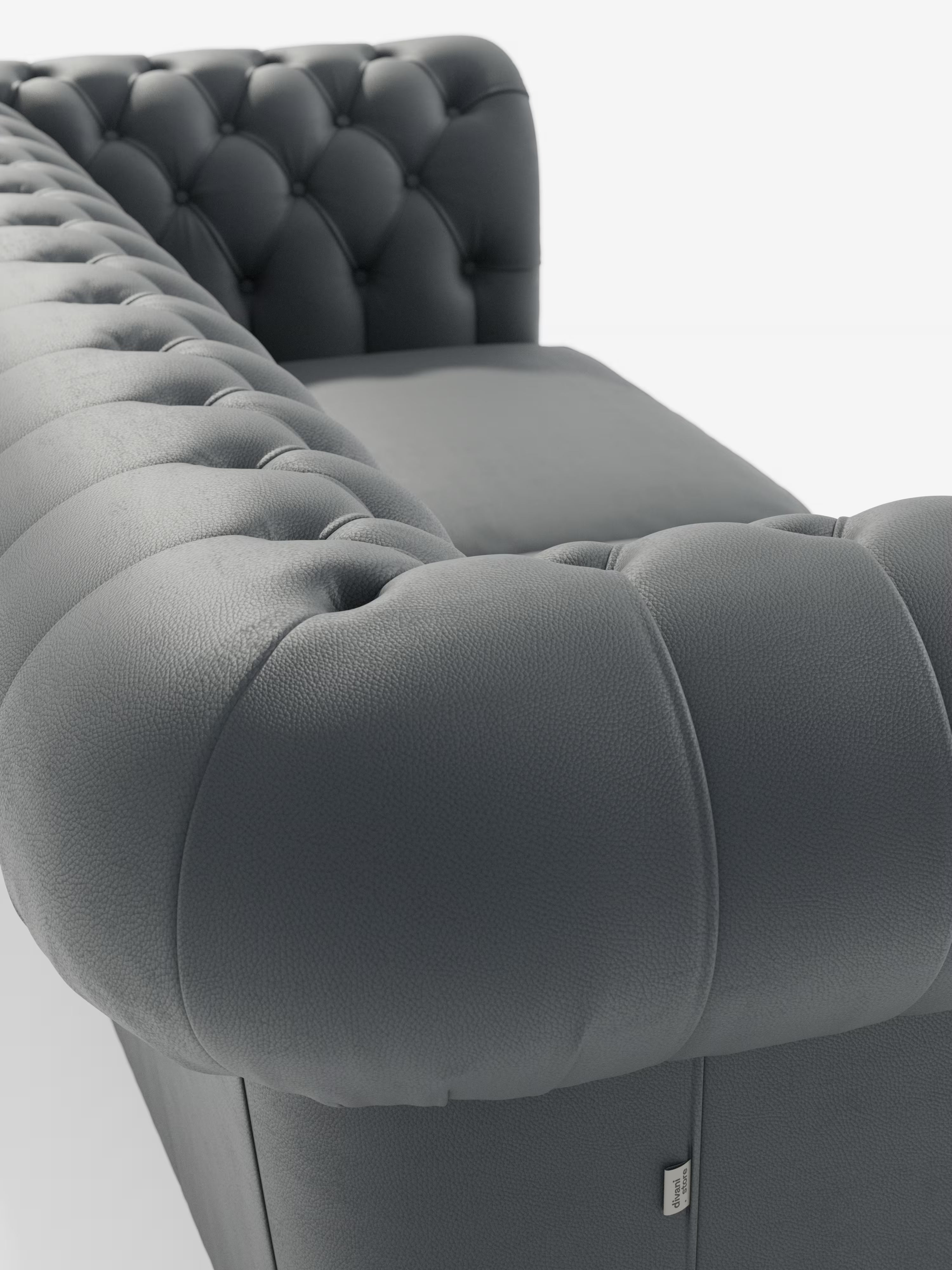 Primo piano del moderno Chester grigio scuro – Divano Chesterfield in vera pelle spessorata a 2 e 3 posti di Divani.Store, che mette in risalto la profonda trapuntatura a bottoni sui braccioli arrotondati e sullo schienale. È visibile la ricca trama della vera pelle spessorata, con una piccola etichetta in tessuto applicata sul lato inferiore. Questo elegante divano artigianale Made in Italy è presentato su uno sfondo bianco a tinta unita.