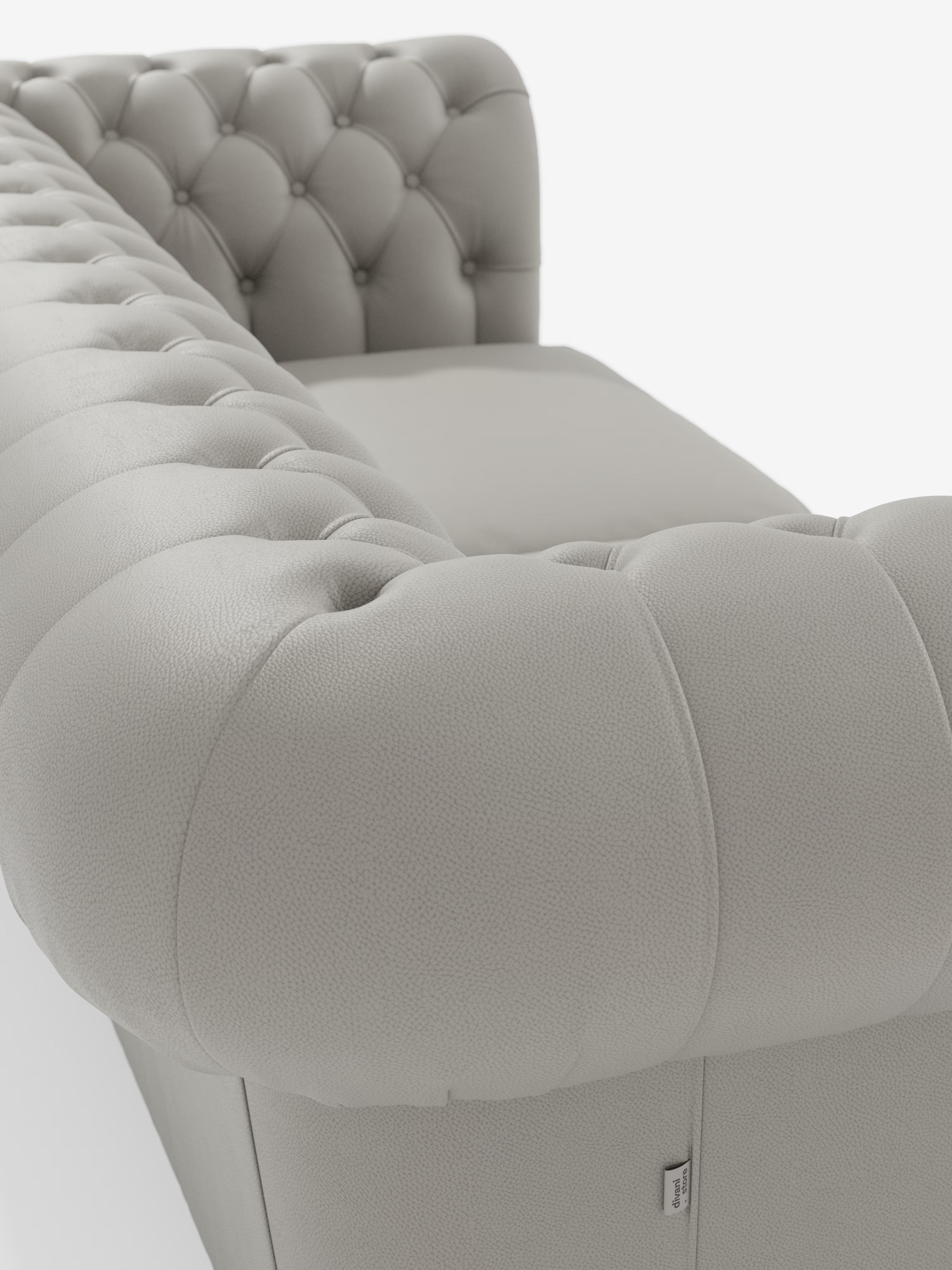 Primo piano del Chester – Divano Chesterfield in vera pelle spessorata a 2 e 3 posti di Divani.Store, caratterizzato da un rivestimento in pelle grigio chiaro trapuntata con profondi bottoni decorativi sui braccioli e sullo schienale. La prospettiva angolata mette in risalto la morbida consistenza del divano e la lussuosa finitura in vera pelle su uno sfondo bianco.