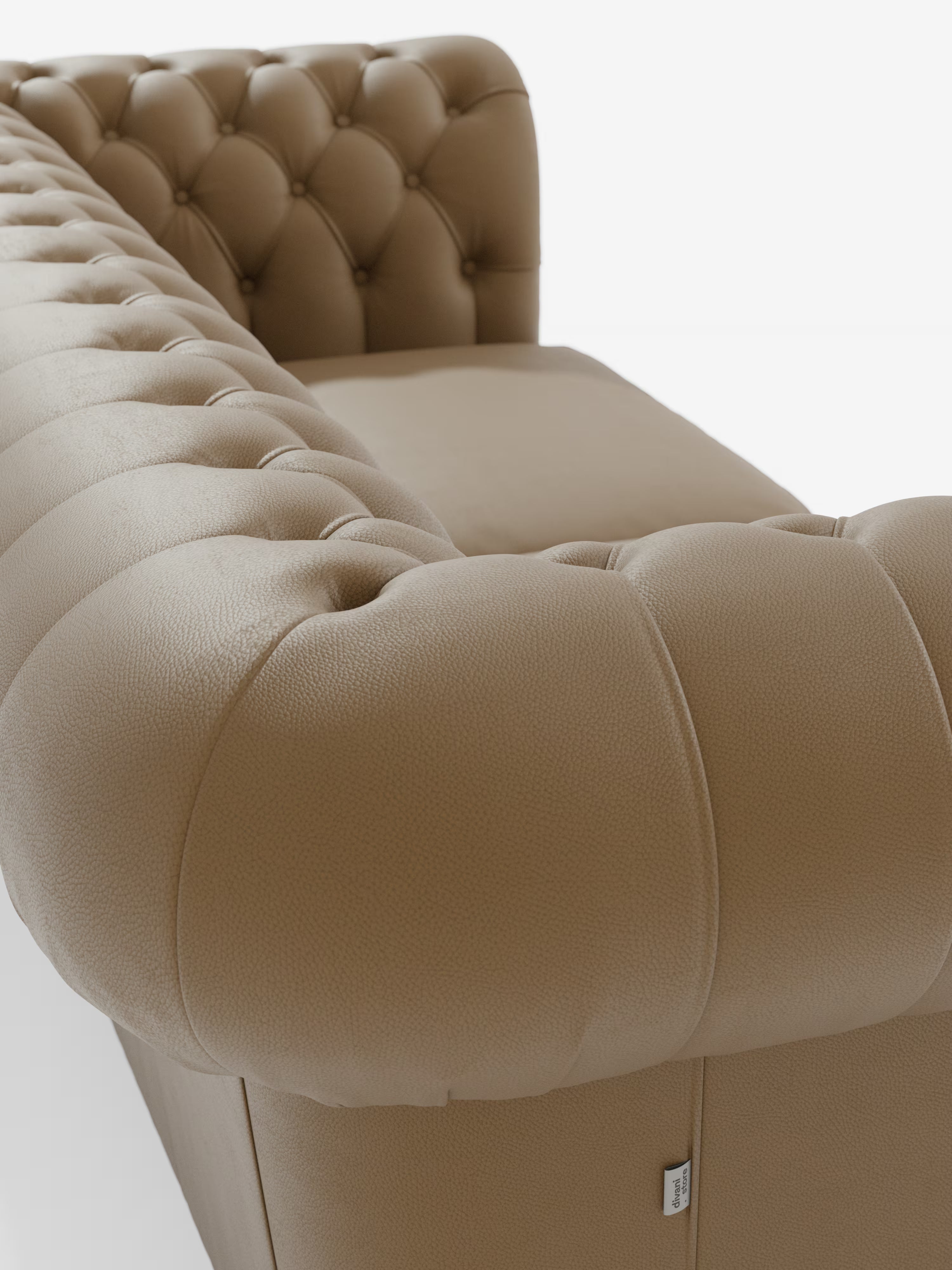 Primo piano del “Chester – Divano Chesterfield in vera pelle spessorata a 2 e 3 posti” di Divani.Store, caratterizzato da un rivestimento in pelle color cuoio con trapuntatura, braccioli arrotondati e cuscino di seduta liscio, su sfondo bianco. La ricca trama della vera pelle spessorata e i dettagli della trapuntatura a bottoni sono chiaramente in evidenza, sottolineando l’eleganza classica di questo divano Chesterfield. Sul lato è apposta una piccola etichetta in tessuto bianco.