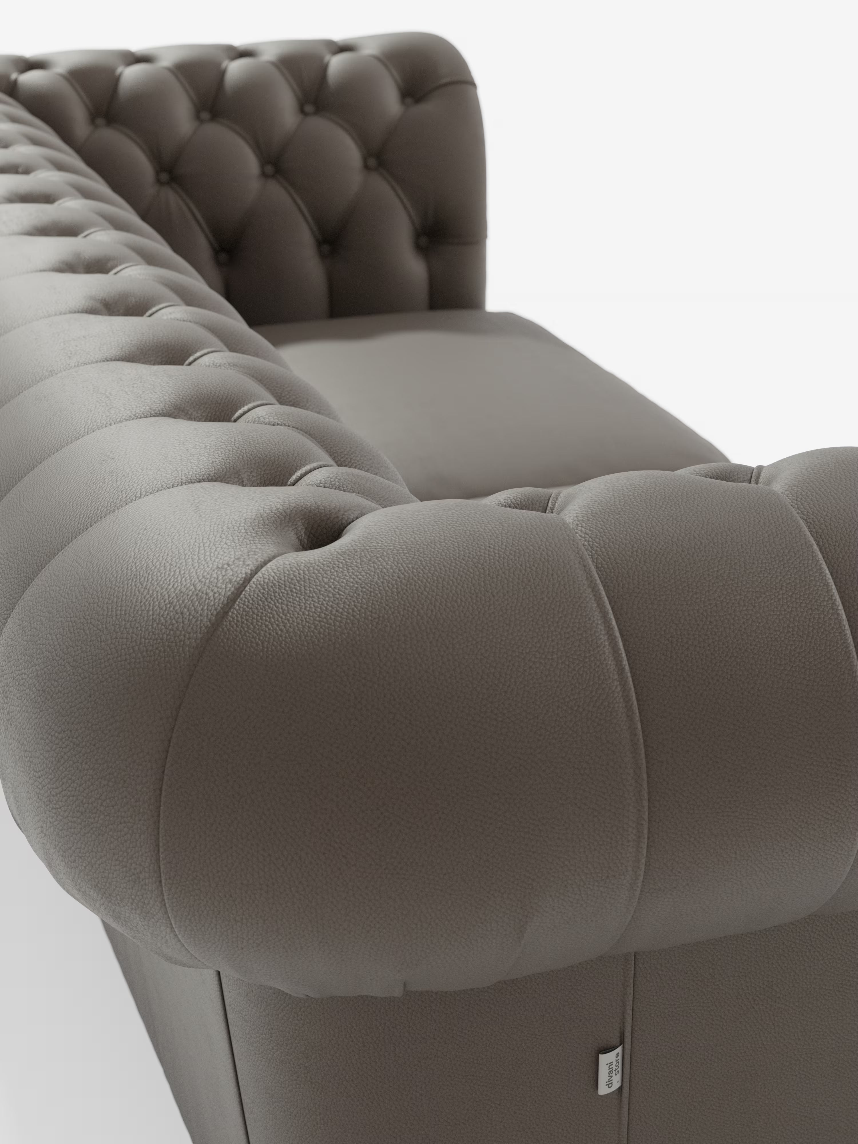 Primo piano del Chester – Divano Chesterfield in vera pelle spessorata a 2 e 3 posti di Divani.Store, che mette in risalto il rivestimento in pelle marrone trapuntata con profondi bottoni sia sullo schienale che sui braccioli. Questo divano artigianale Made in Italy è realizzato in vera pelle liscia di alta qualità e presenta una piccola etichetta in tessuto bianco nella parte inferiore del divano. Lo sfondo è bianco a tinta unita.