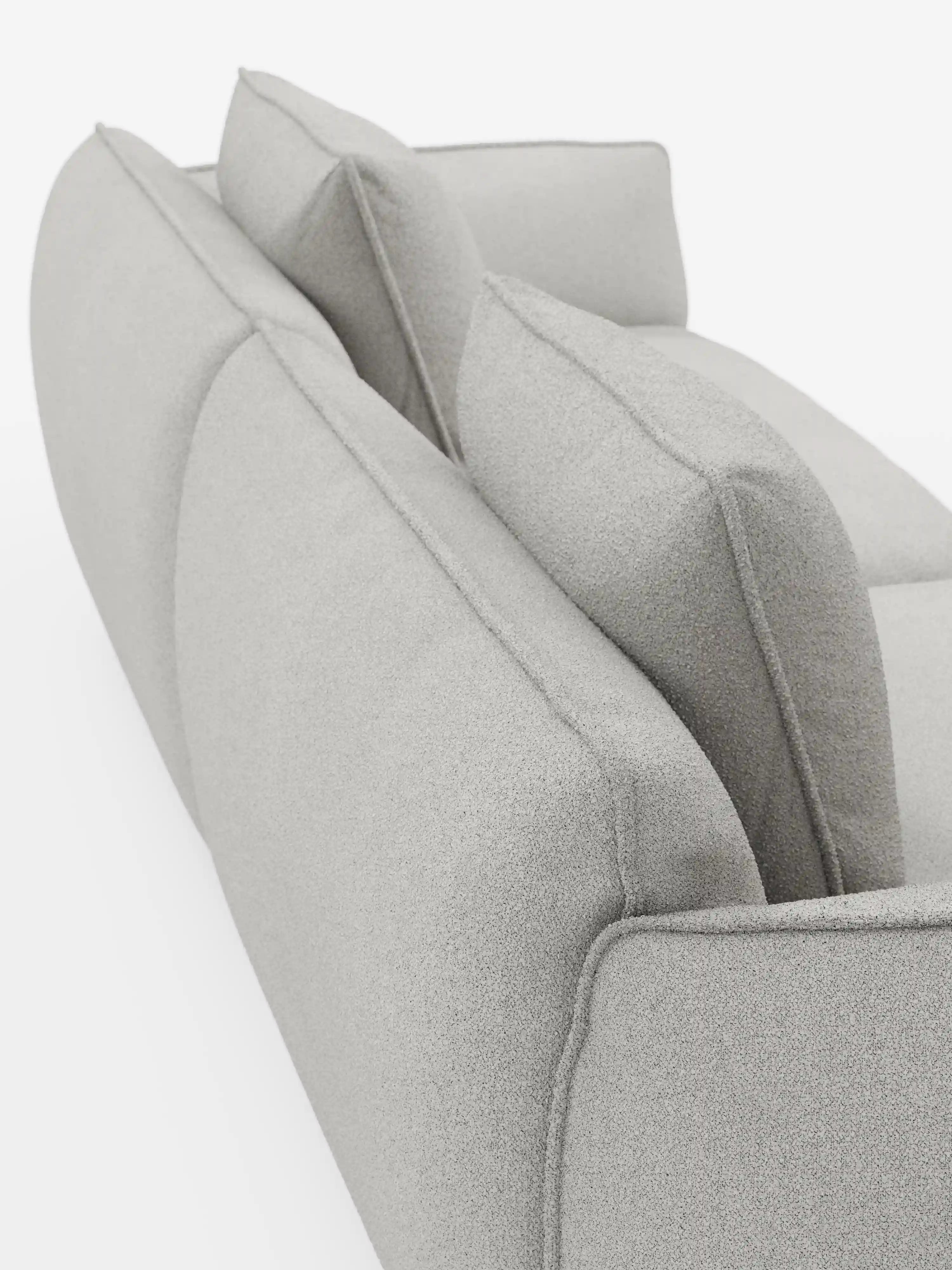 Primo piano con inquadratura angolare del divano modulare e componibile a 3 posti Nimbus da 250 cm di Divani.Store in grigio chiaro, caratterizzato da cuciture pulite e dal tessuto T33 effetto cotone, testurizzato e resistente alle macchie. L'immagine mette in risalto lo schienale e il bracciolo del divano con due cuscini quadrati su uno sfondo bianco.
