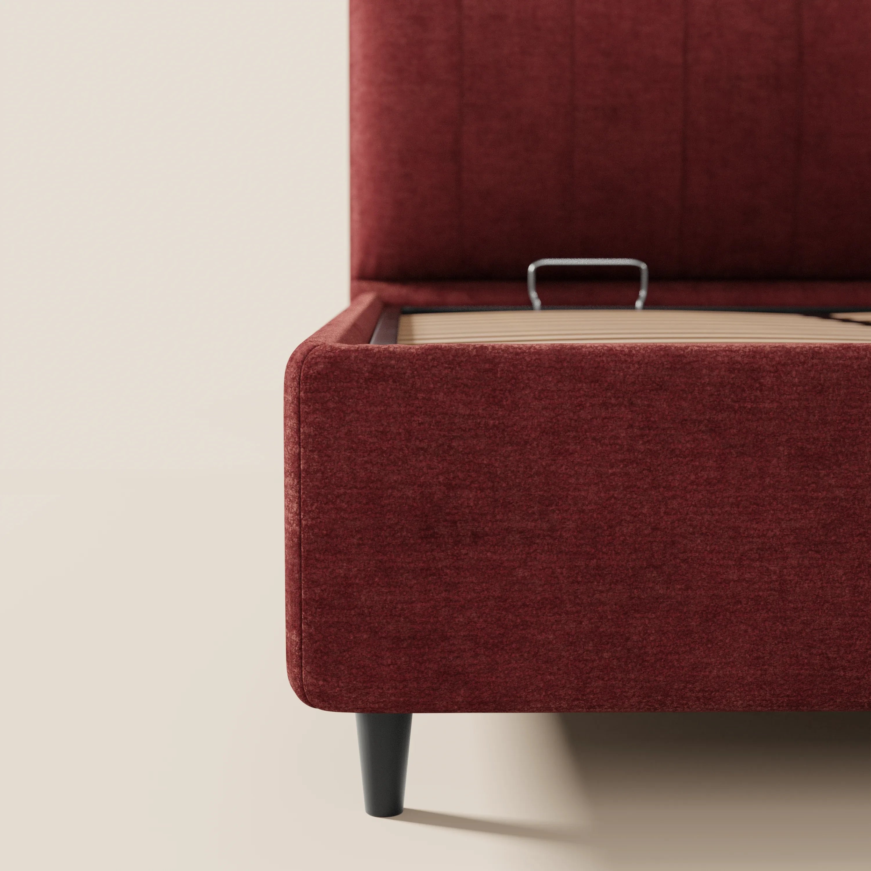 Un primo piano del letto imbottito con contenitore ONYX di Letti.store mette in risalto la struttura rivestita in tessuto rosso intenso certificato Oeko-Tex®, le gambe nere e la base parzialmente aperta che lascia intravedere una maniglia in metallo. Lo sfondo chiaro permette di mettere in risalto il suo design moderno.