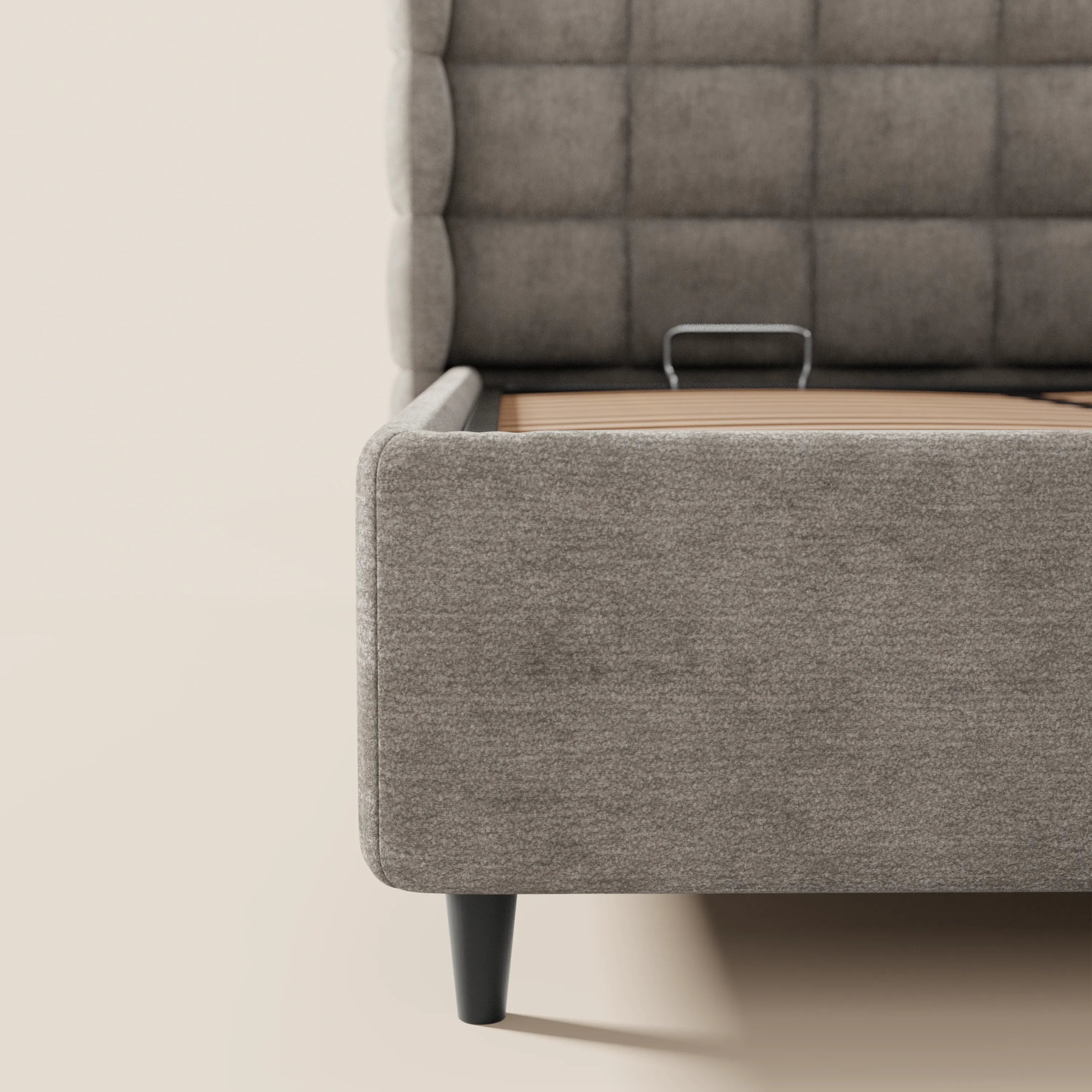 Primo piano del letto imbottito RAGNAR di Letti.store, realizzato in morbido tessuto grigio certificato Oeko-Tex®, caratterizzato da un'alta testiera avvolgente capitonné con motivi quadrati e gambe affusolate nere. Il materasso è assente, lasciando a vista la struttura portante del contenitore.