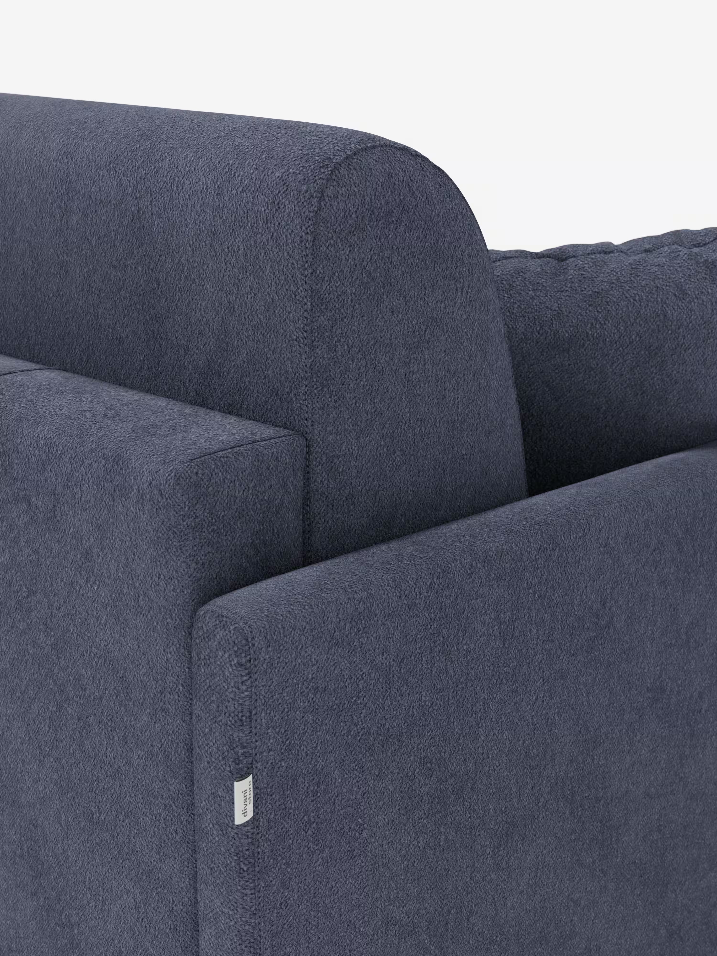 Primo piano di un moderno divano letto Tommy Divano a 2 e 3 posti matrimoniale, colore blu scuro, di Divani.Store, caratterizzato da braccioli sottili e schienale dalle linee pulite. Sul bracciolo è apposta una piccola etichetta in tessuto bianco ed è visibile il rivestimento in simil cotone T33, testurizzato e resistente alle macchie. Lo sfondo è bianco a tinta unita.
