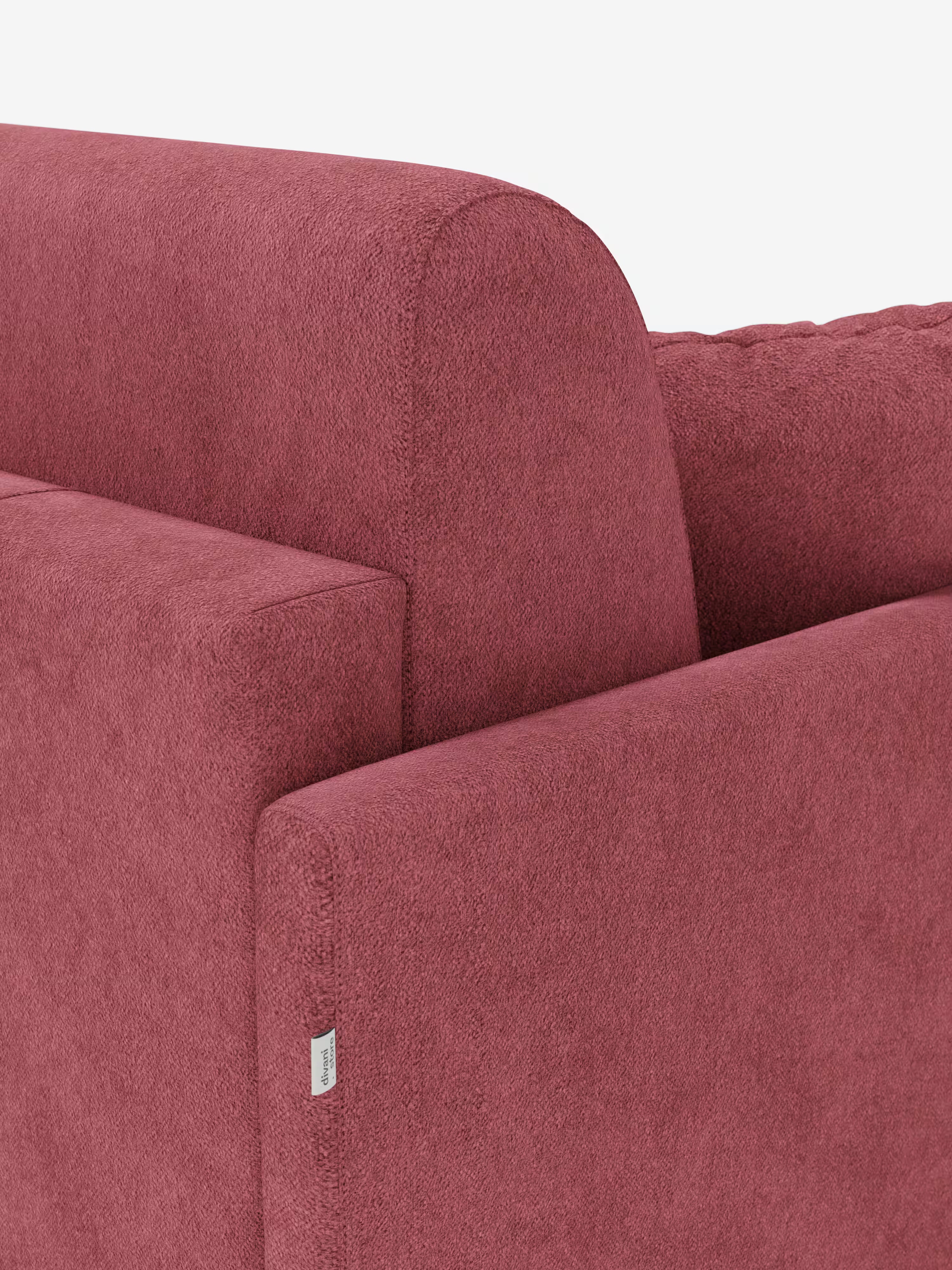 Primo piano dell'angolo di un moderno divano letto Tommy Divano a 2 e 3 posti matrimoniale di Divani.Store, sfoderabile al 100% e rivestito in tessuto T33 effetto cotone, rosso tenue, testurizzato e antimacchia. L'immagine mette in risalto lo schienale e il bracciolo sottile dalle linee pulite, oltre a una piccola etichetta in tessuto bianco applicata vicino alla cucitura del bracciolo. Il tutto su uno sfondo bianco a tinta unita.