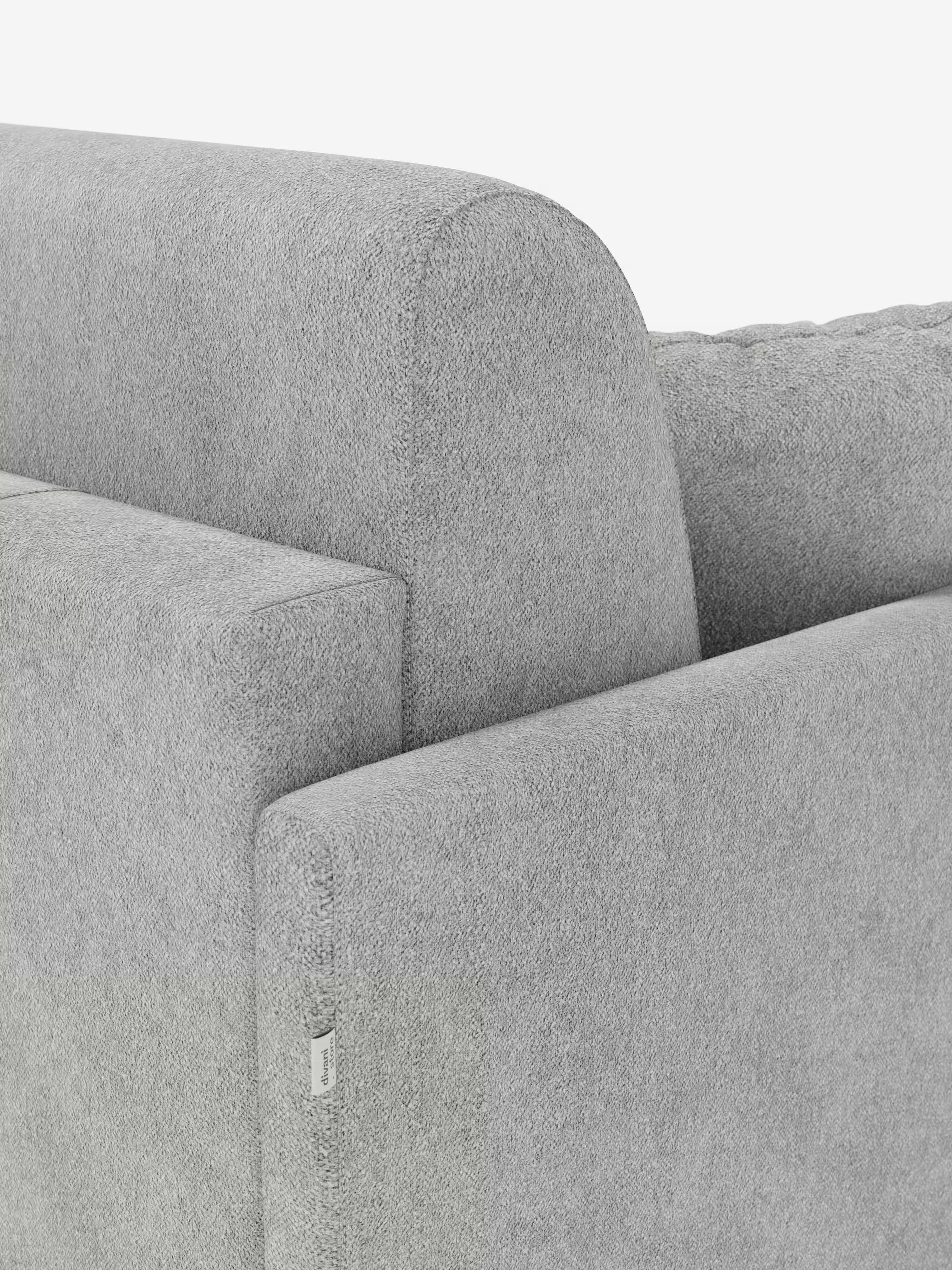 Primo piano del divano letto Tommy Divano a 2 e 3 posti matrimoniale di Divani.Store, un moderno divano letto grigio chiaro realizzato in tessuto T33, simile al cotone, facile da pulire e completamente sfoderabile. L'immagine si concentra sul bracciolo e sullo schienale, mettendo in risalto il rivestimento morbido e testurizzato e una piccola etichetta in tessuto bianco sul bracciolo. Lo sfondo è bianco a tinta unita.