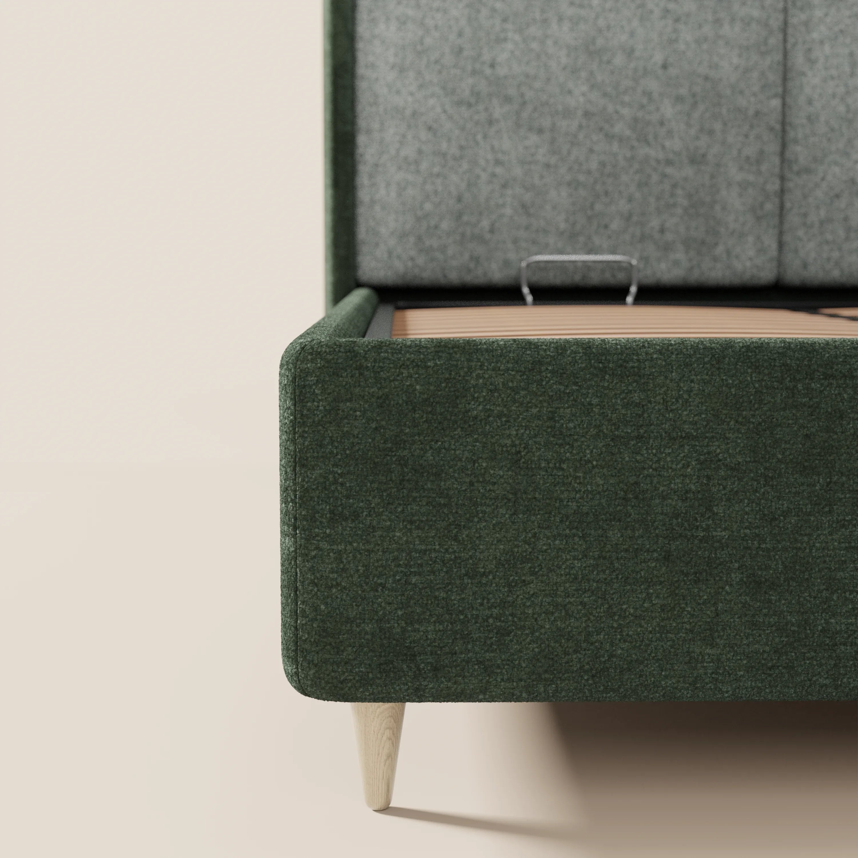 Un primo piano del letto imbottito bicolore VALKIRIA di Letti.store ne mette in risalto il tessuto verde scuro, la testiera curva imbottita di colore grigio, le gambe in legno chiaro e un vano contenitore parzialmente aperto con maniglia interna in metallo. Lo sfondo è semplice e chiaro.