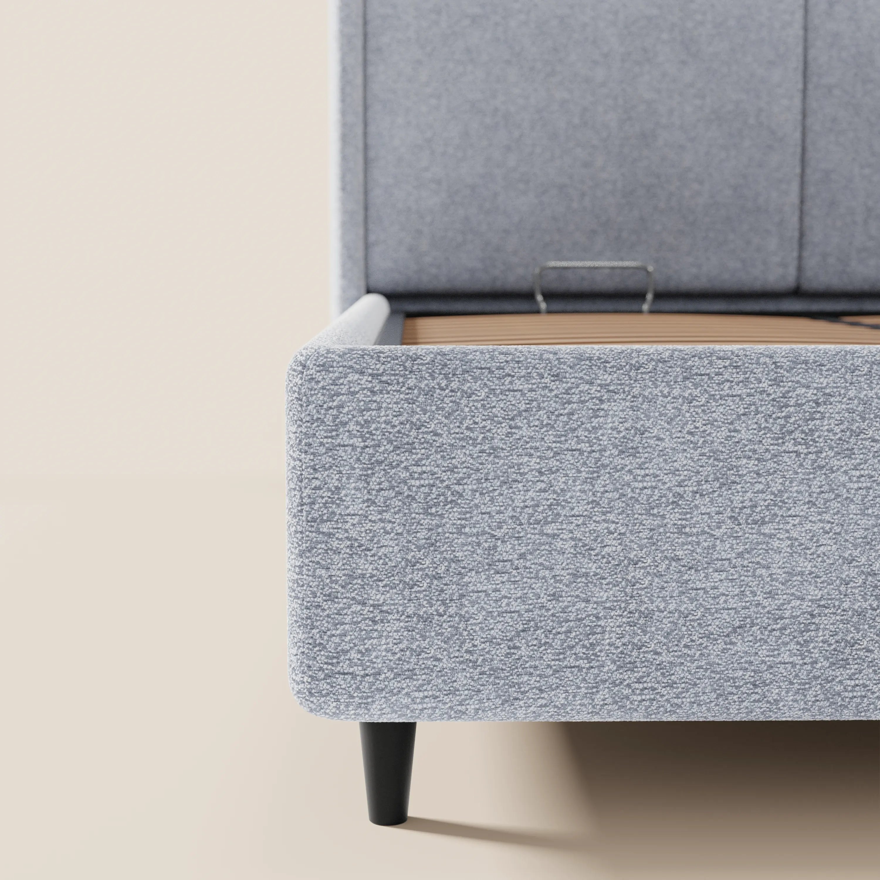 Primo piano del letto di design VALKIRIA di Letti.store: tessuto grigio chiaro certificato Oeko-Tex®, testiera alta e avvolgente con 2 cuscini imbottiti, gambe affusolate nere, doghe in legno a vista all’interno. Stile contemporaneo, su sfondo beige.